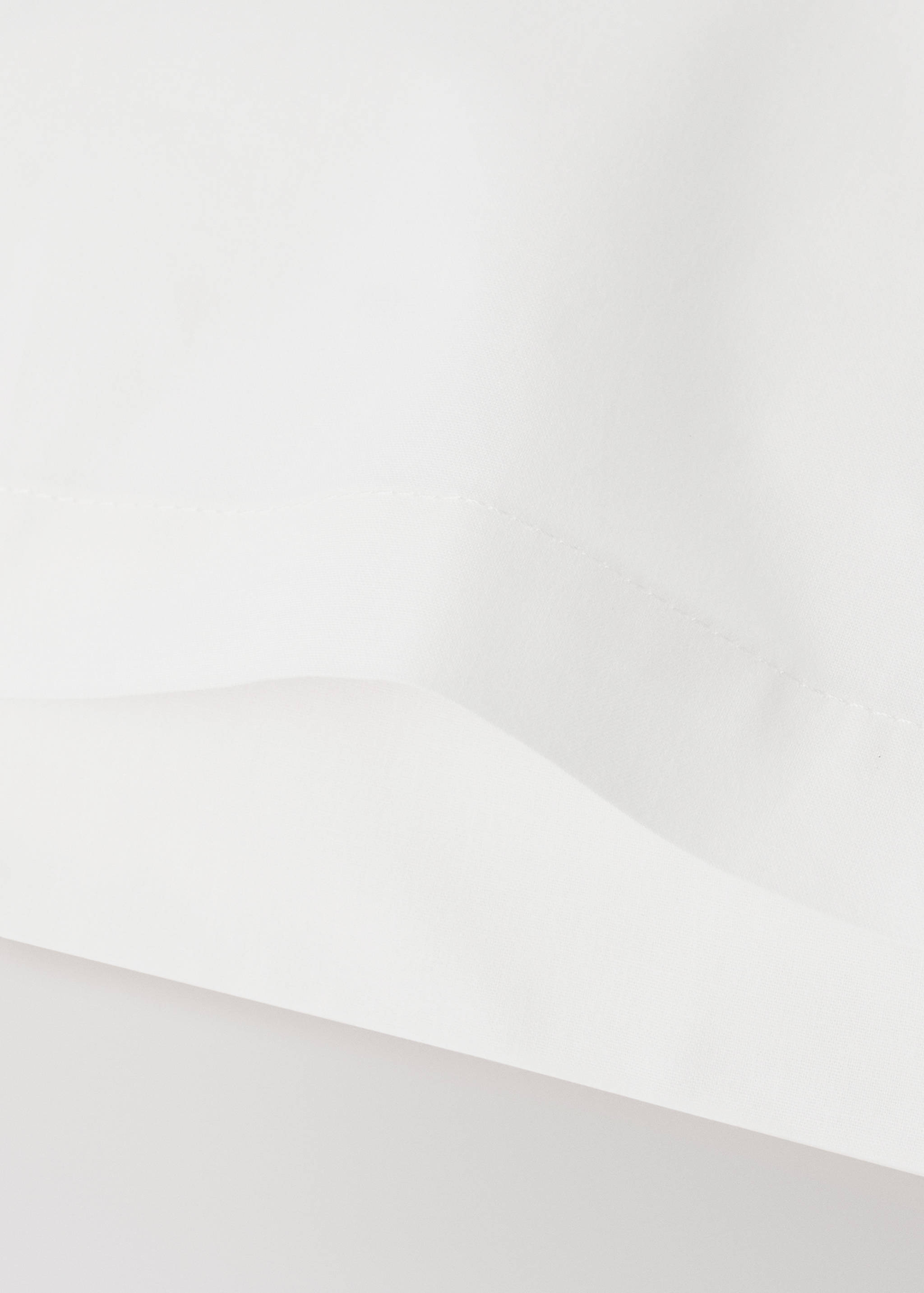 Close-up of a white cot pillowcase showing fabric texture and seams.