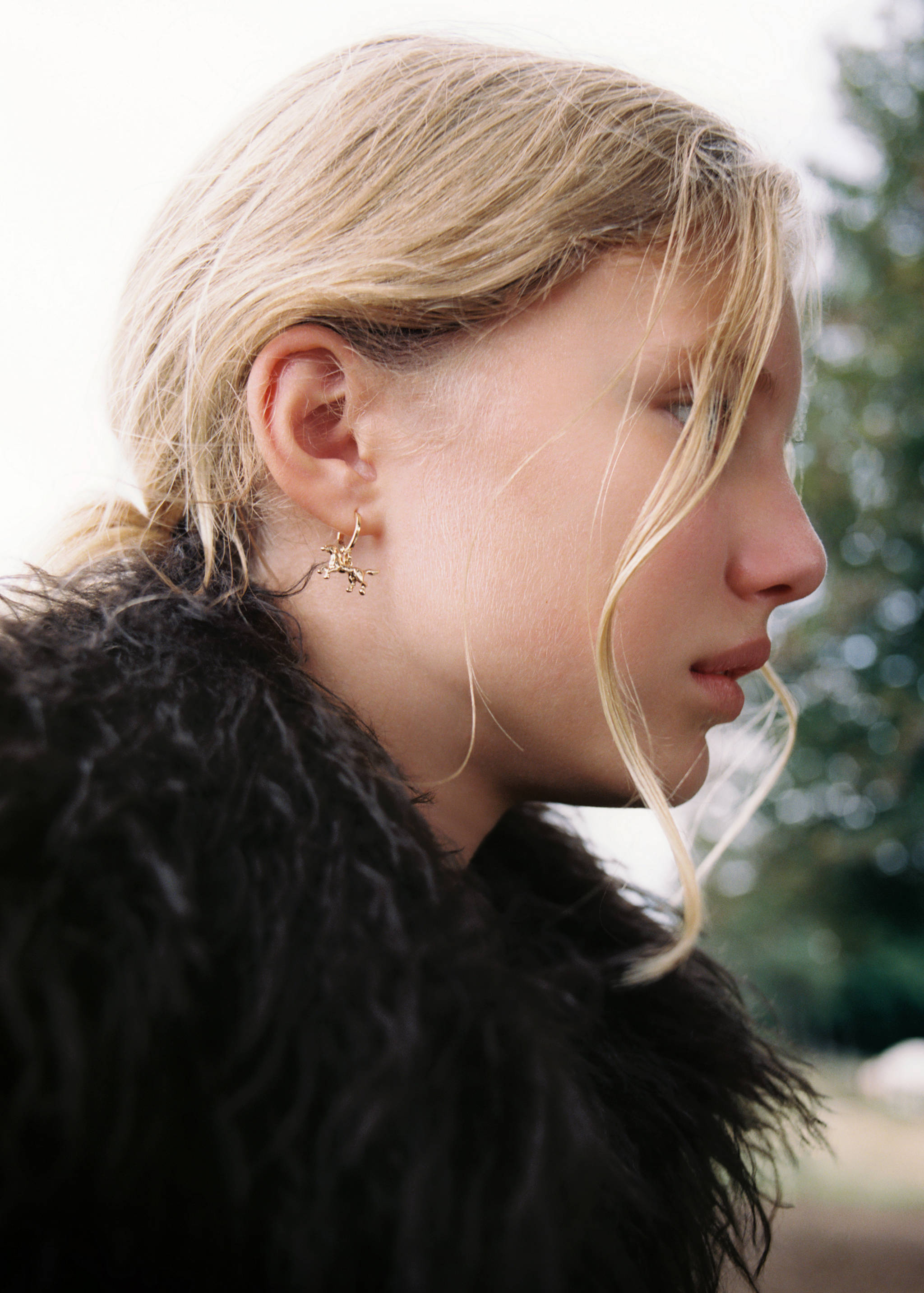 Gold-toned hoop earring with a small horse charm worn by a model.
