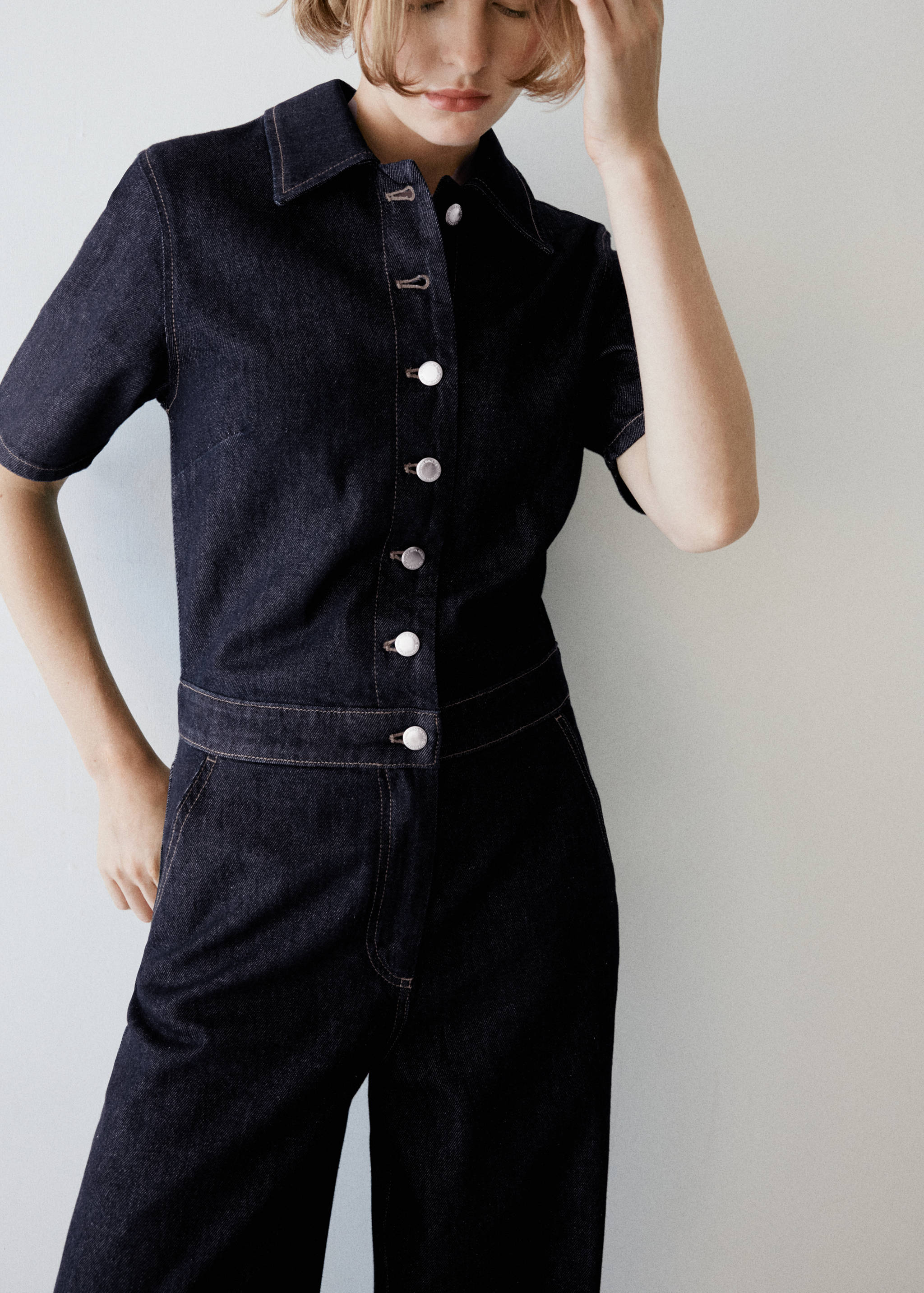 Dark denim short-sleeve jumpsuit with a shirt collar and front metal buttons.