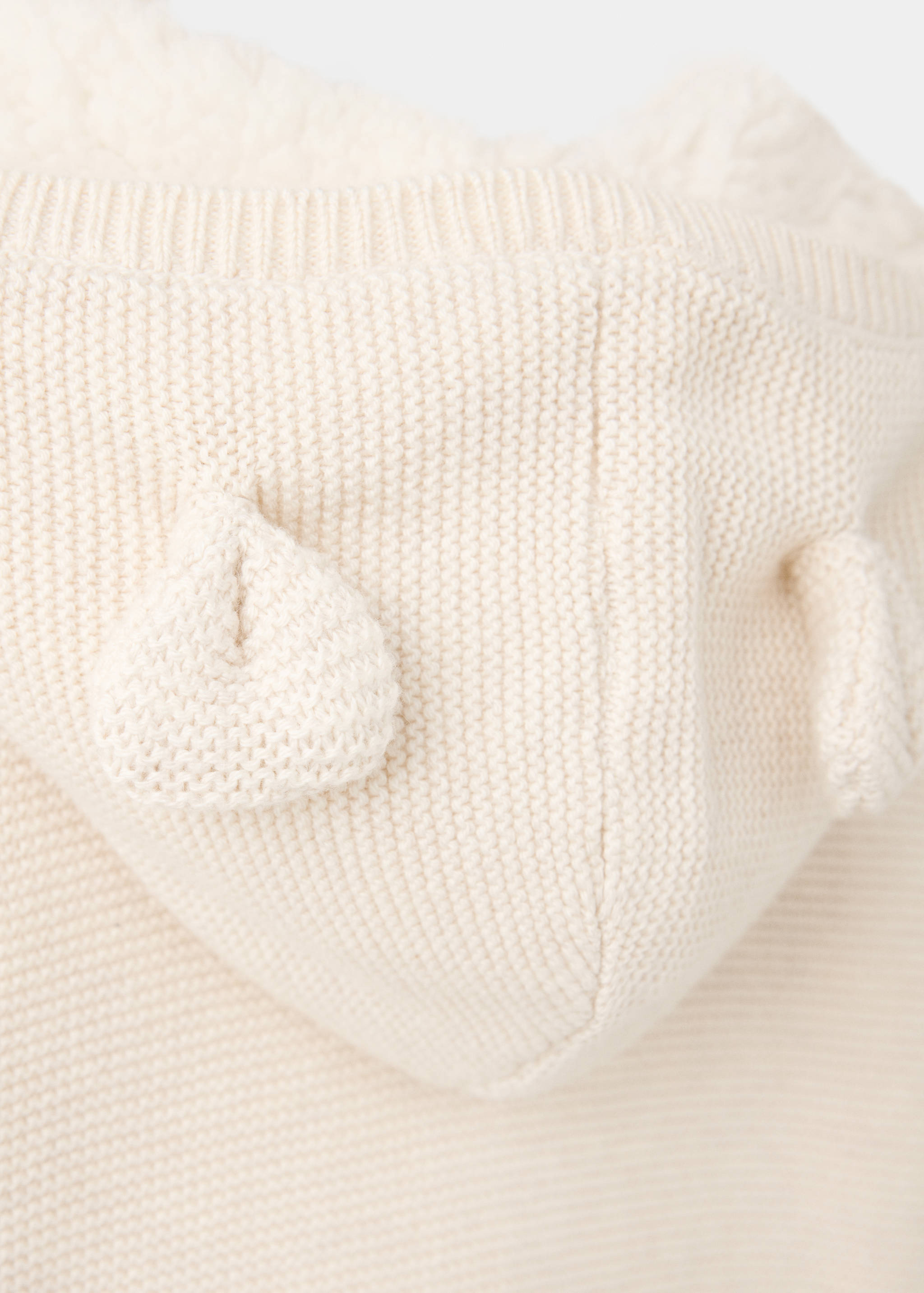 Cream knit cardigan fabric detail showing the textured hood with decorative ears.