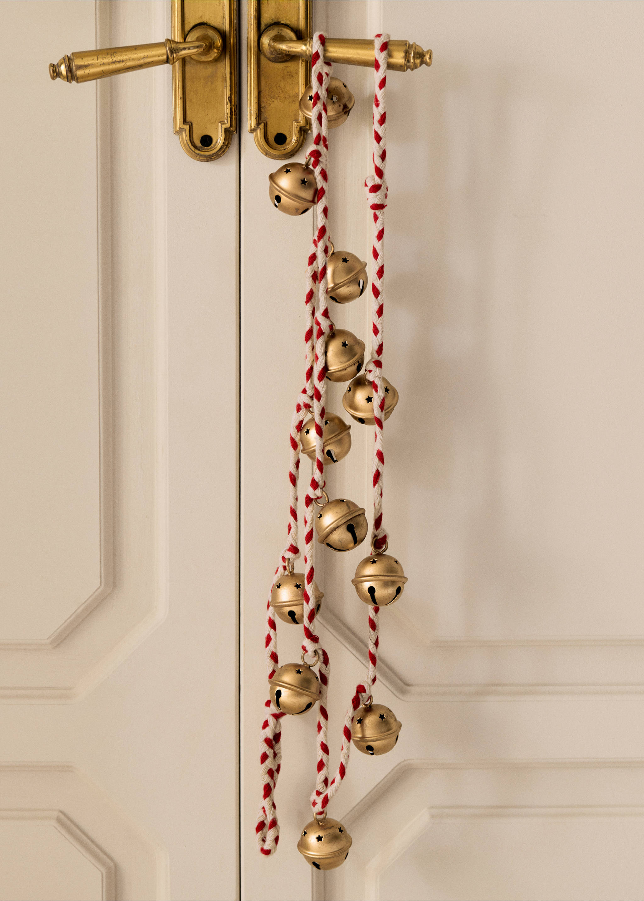Red and white braided cord garland with golden jingle bells, hanging on a door handle., Maroon. Ref: 37076729-00.