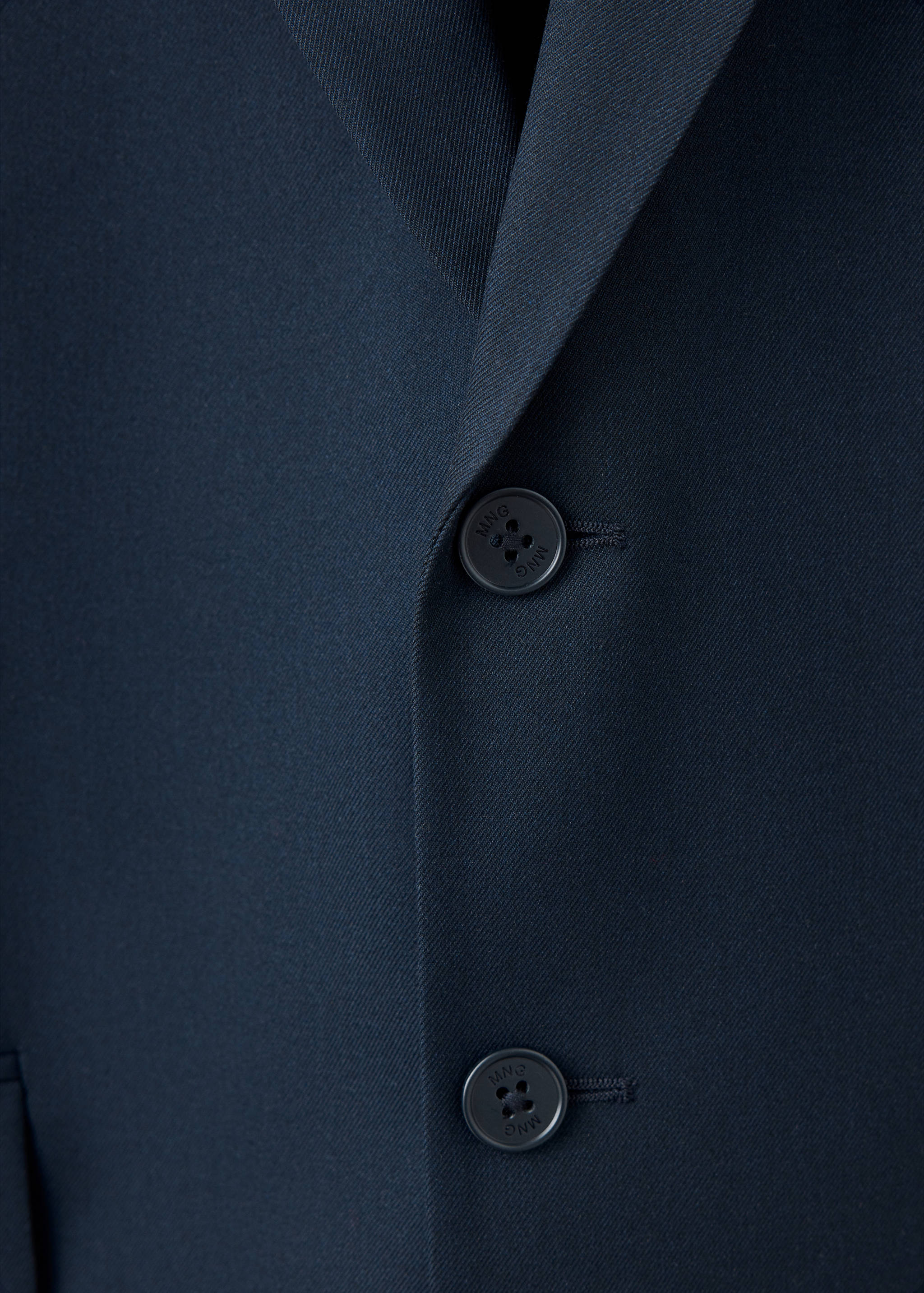 Close-up of a dark navy blue blazer featuring a notched lapel and branded front buttons.