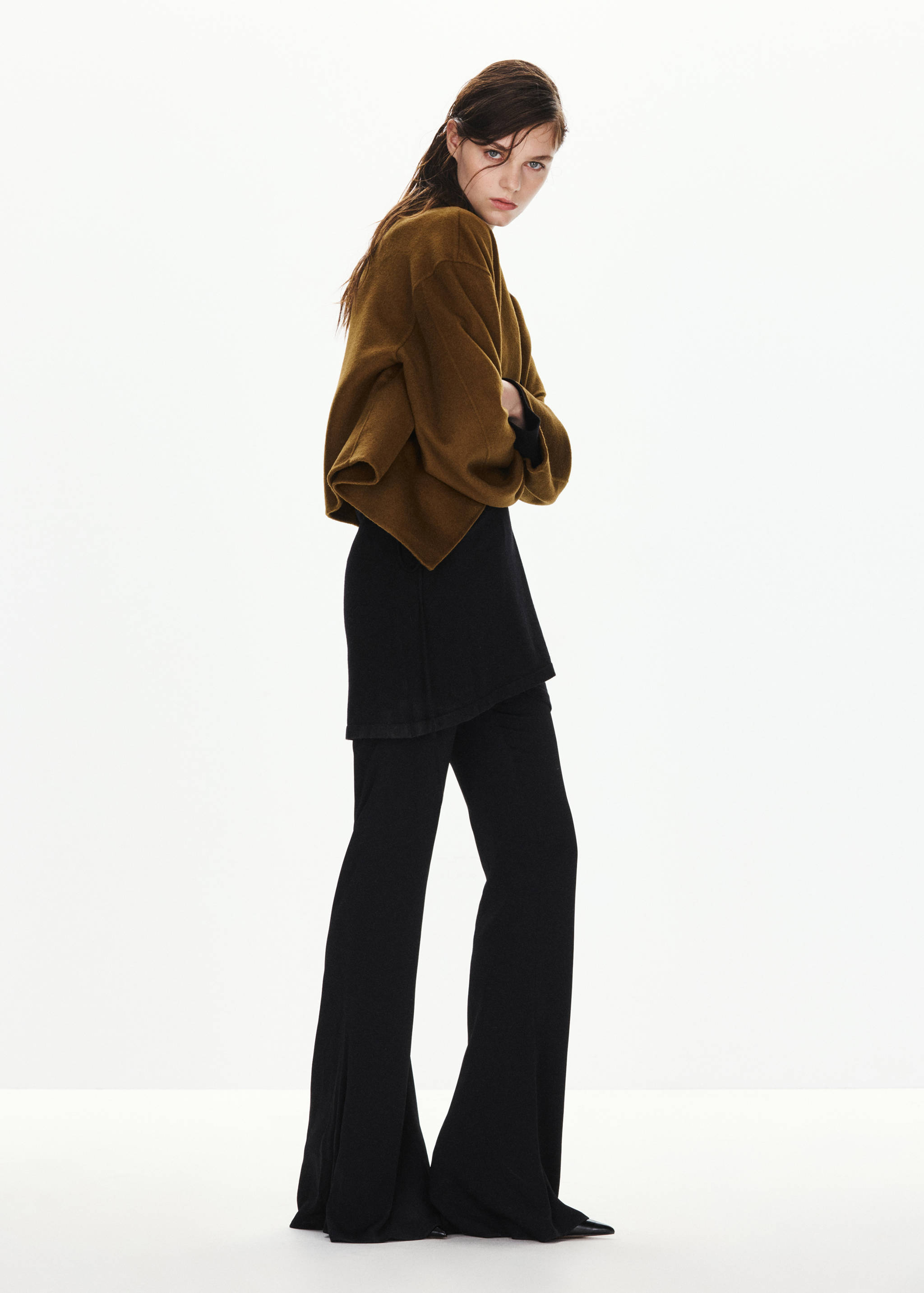 Olive-green cropped jacket with wide sleeves, worn with a black top and flared trousers.