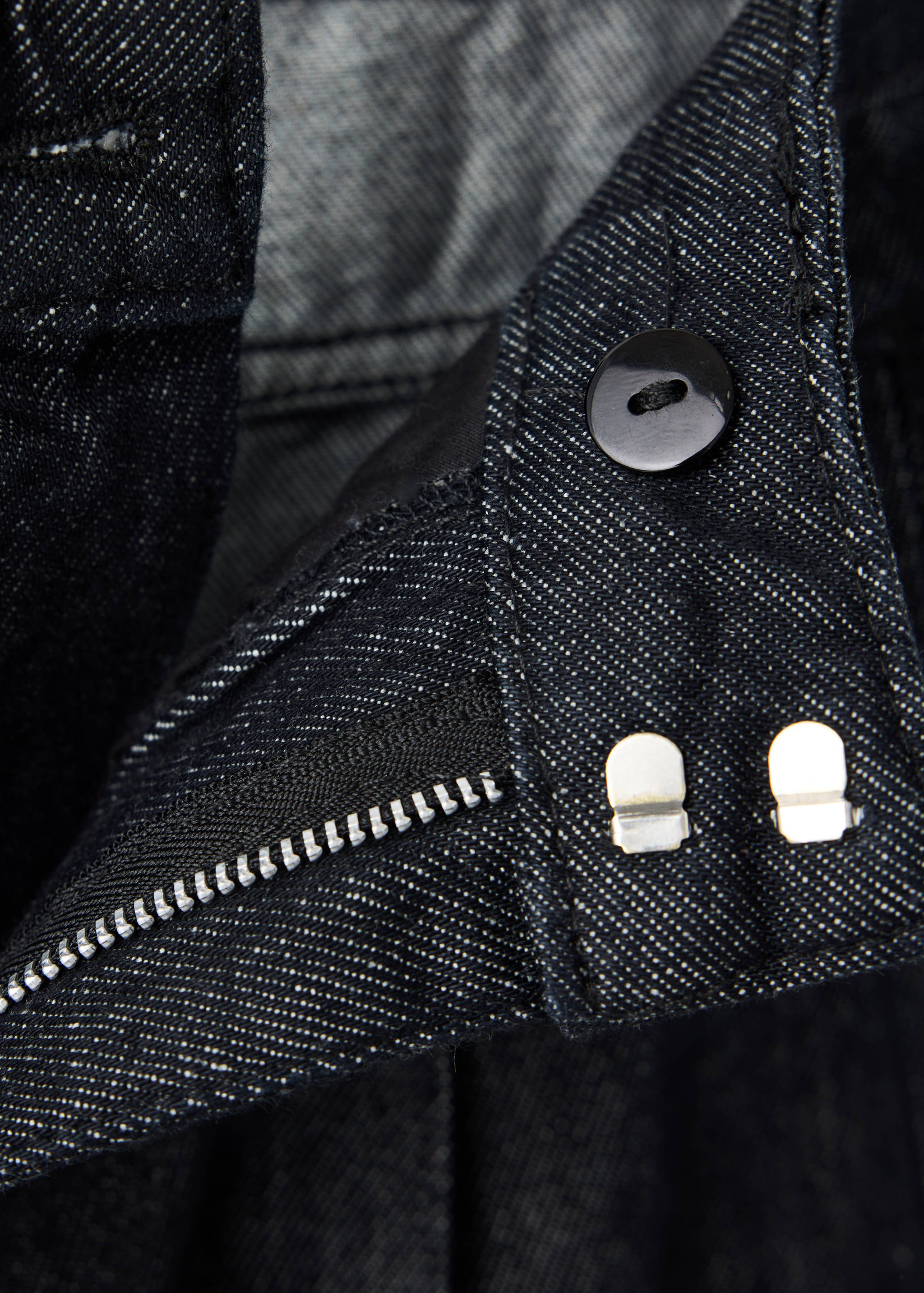 Close-up of dark denim trousers showing the button and zip fastening.