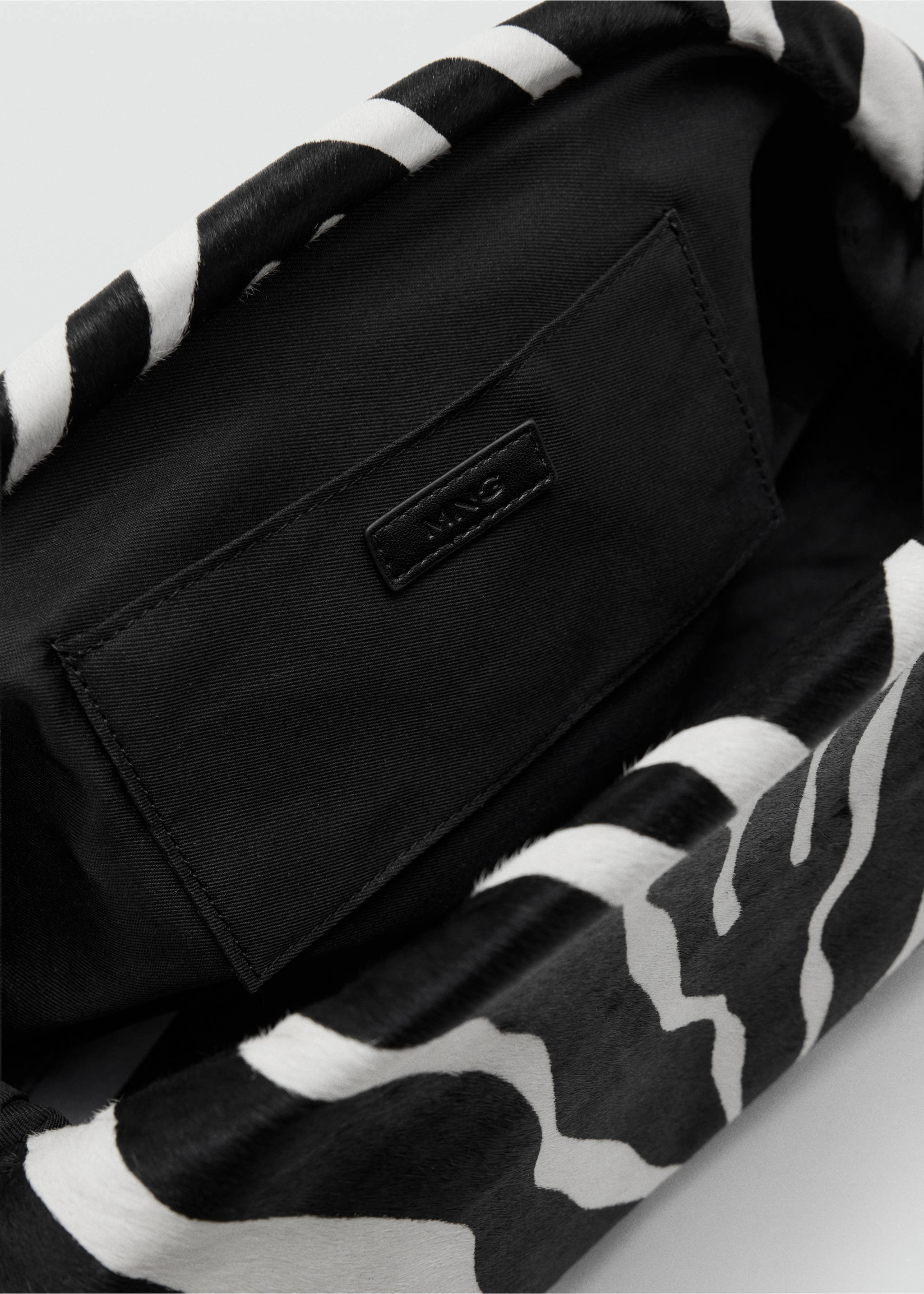 Close-up of a black and white zebra-print handbag interior with black lining and an inner pocket., Black. Ref: 37077133-00.