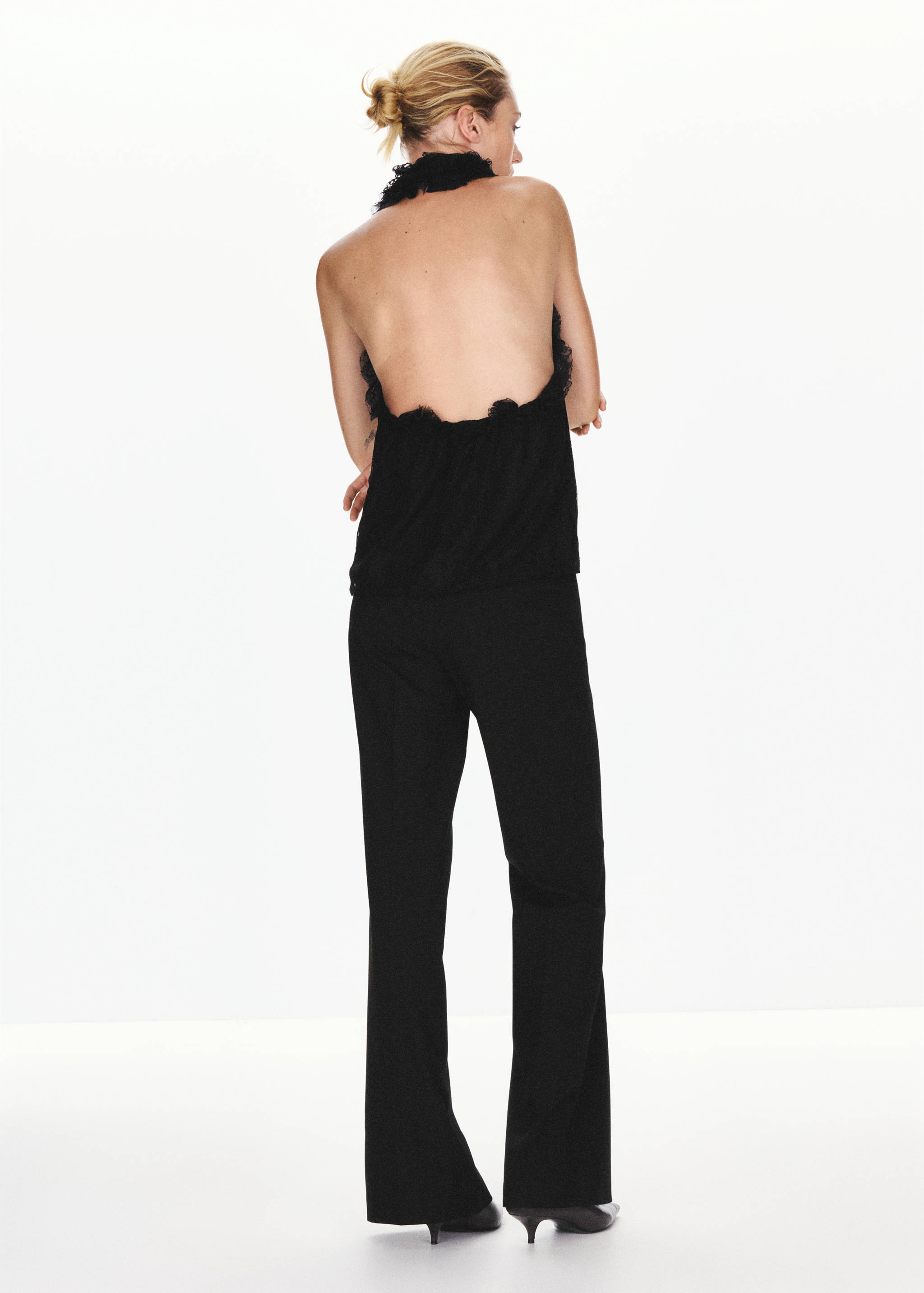 Back view of a black backless halter top with ruffled trim.