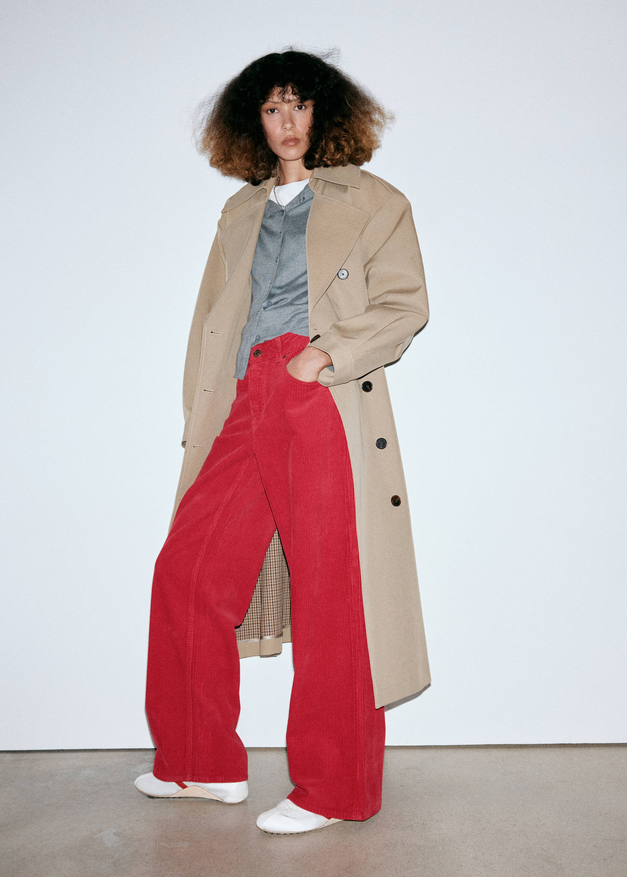 Red wide-leg corduroy trousers worn with a beige trench coat and grey cardigan.