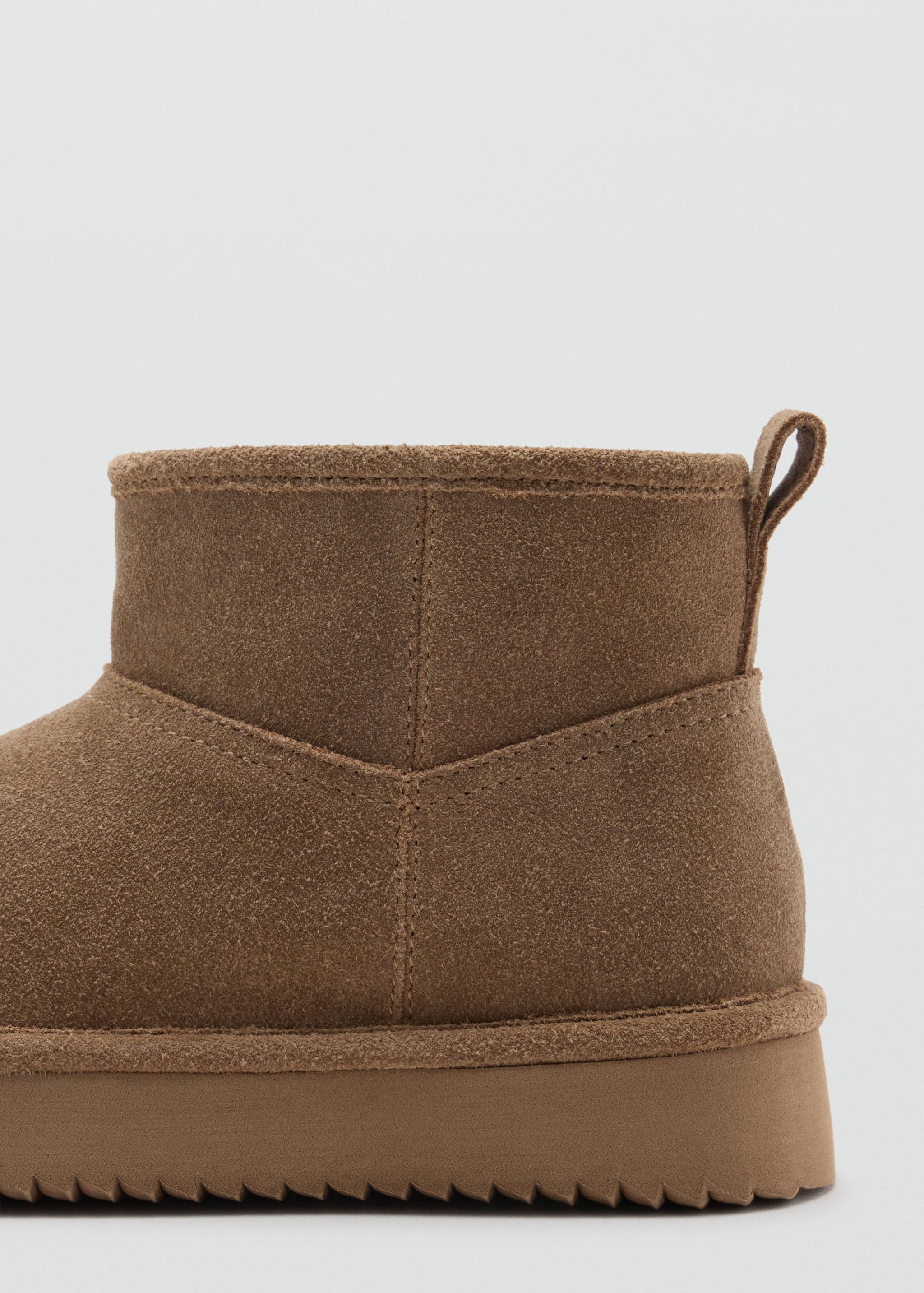 Close-up of a brown suede boot showing the heel detail and pull tab.