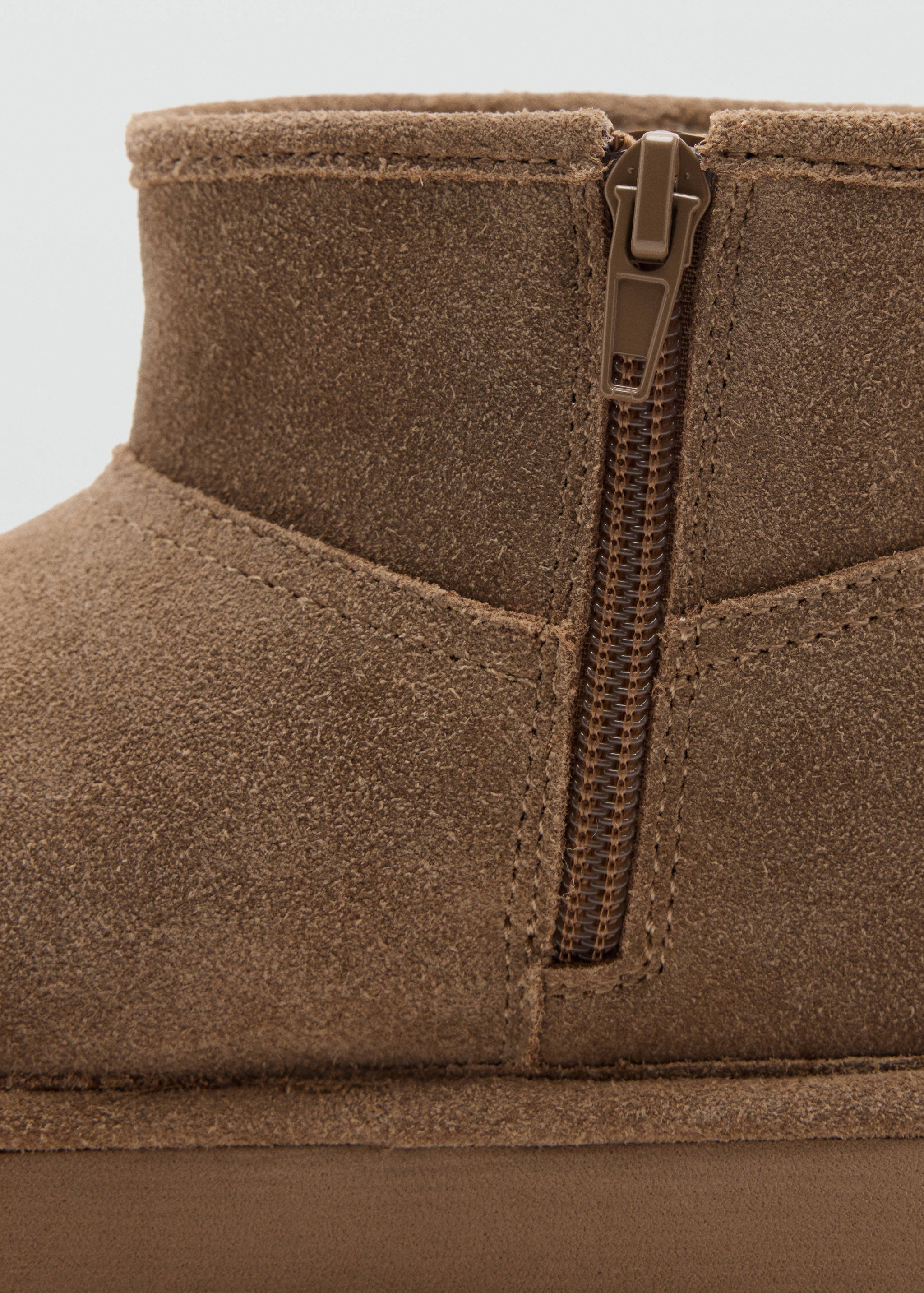 Close-up of brown suede boot showing side zipper detail.