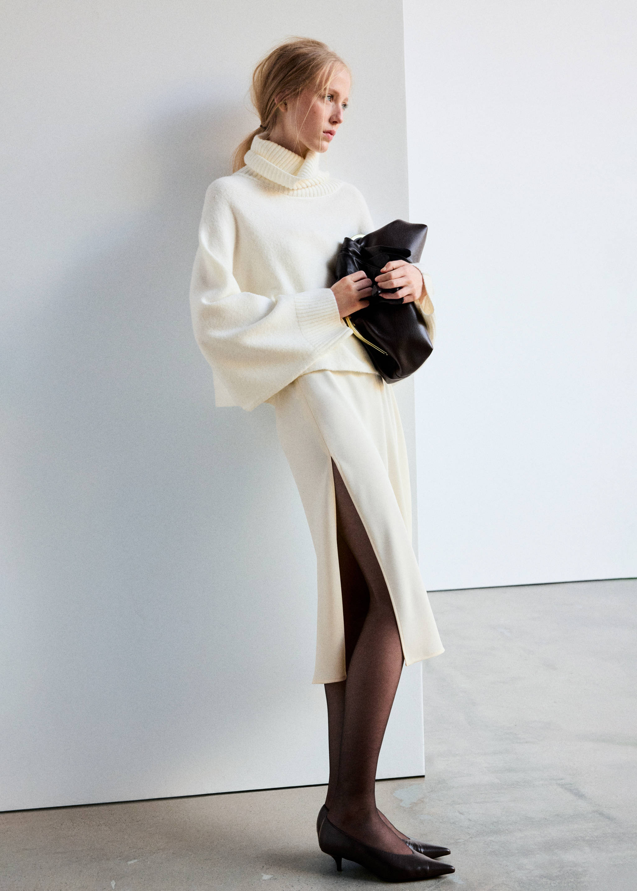 Cream cropped cape with turtleneck and flared sleeves, worn with a matching midi skirt.