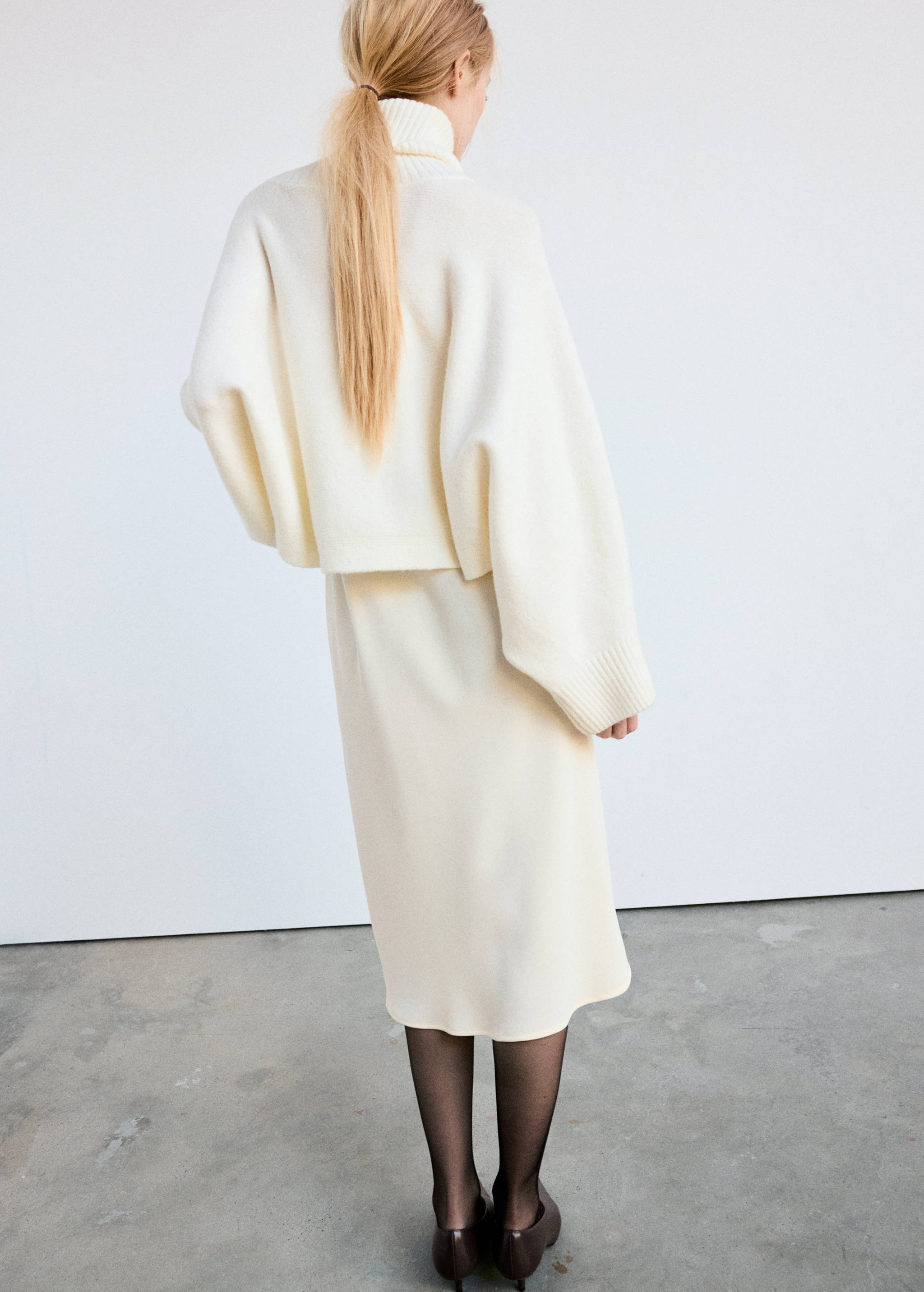 Off-white knitted cape with a high roll neck, back view.