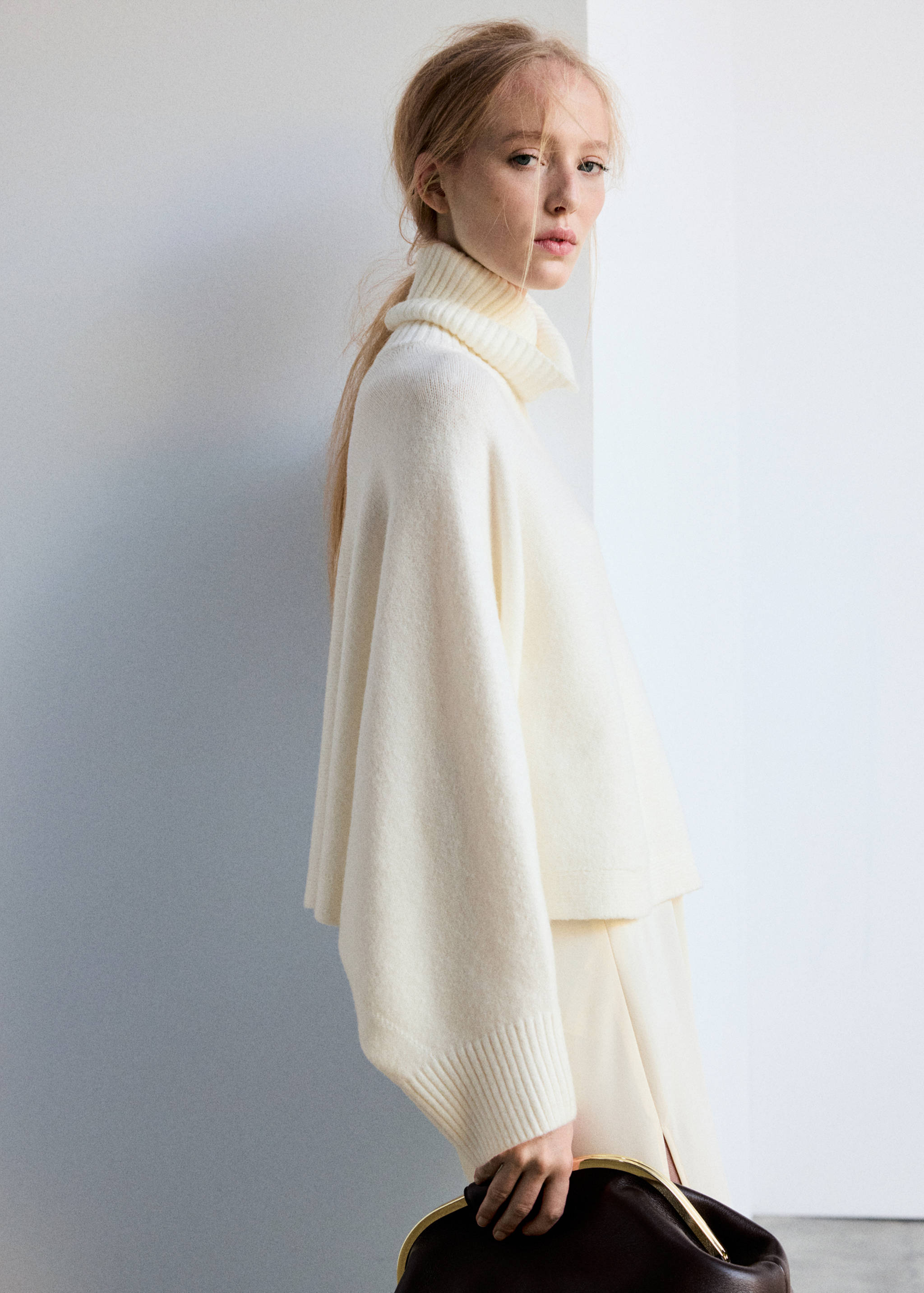 Off-white knitted cape with a roll neck and wide sleeves.