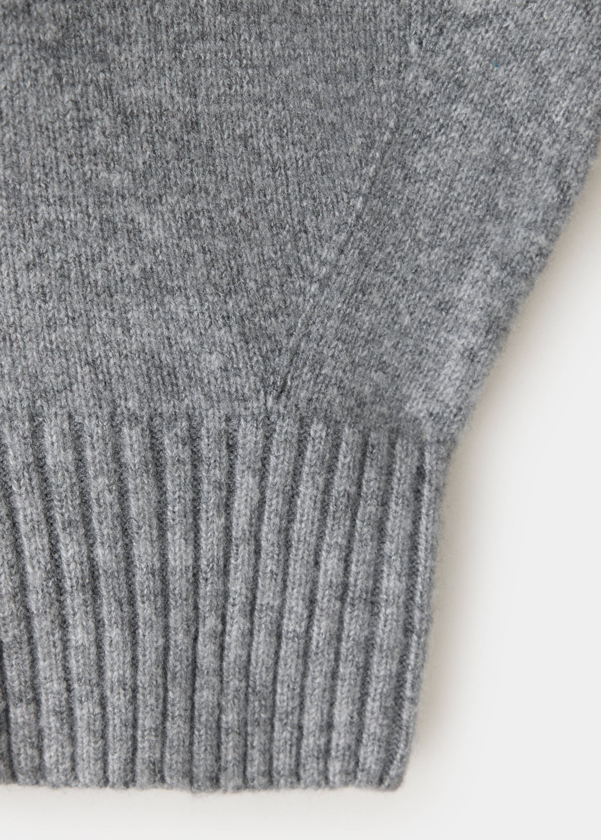 Close-up of the grey knitted fabric and ribbed hem of a cape.