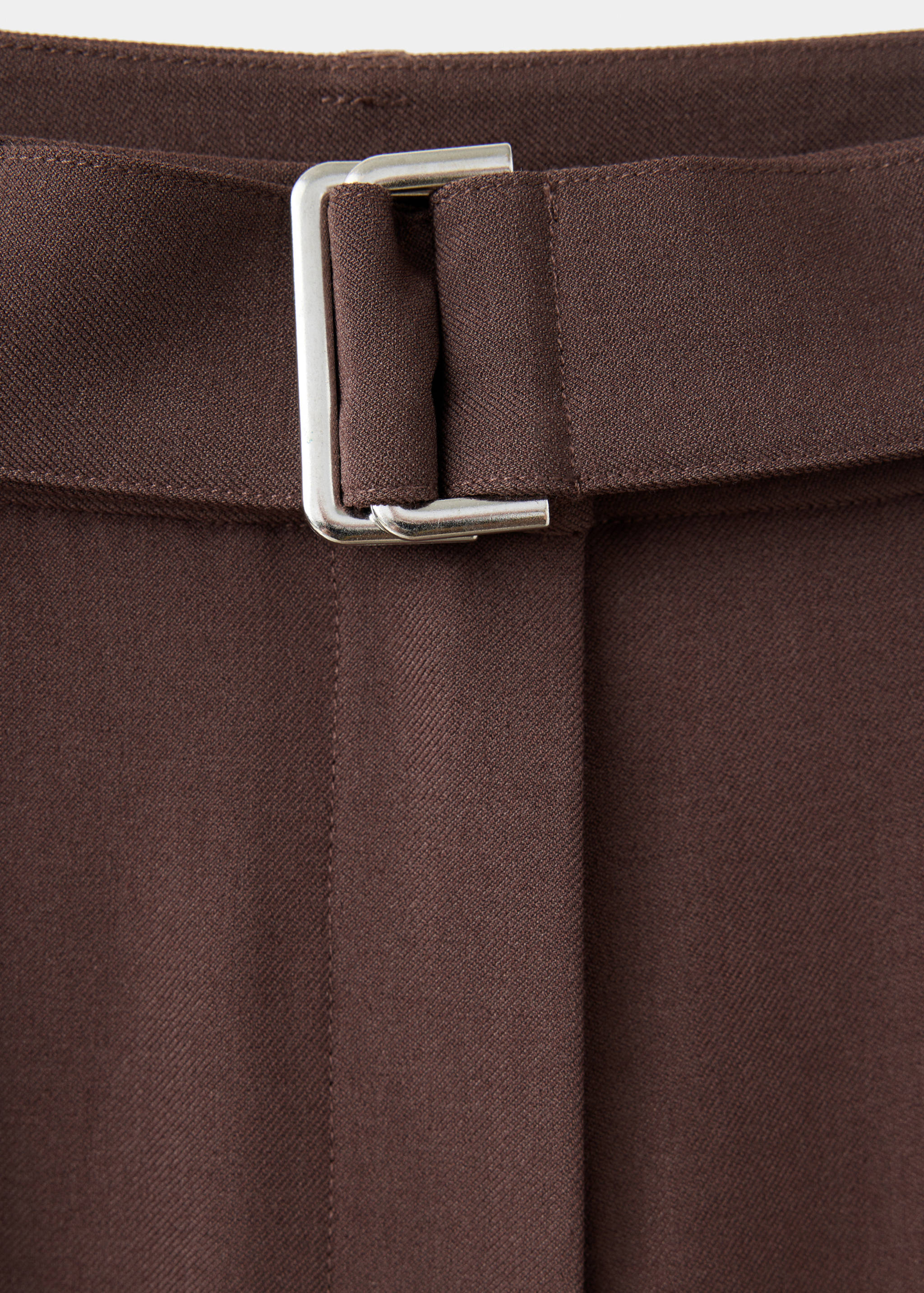 Close-up of brown trousers featuring a matching belt with a silver-tone metal double-ring buckle.