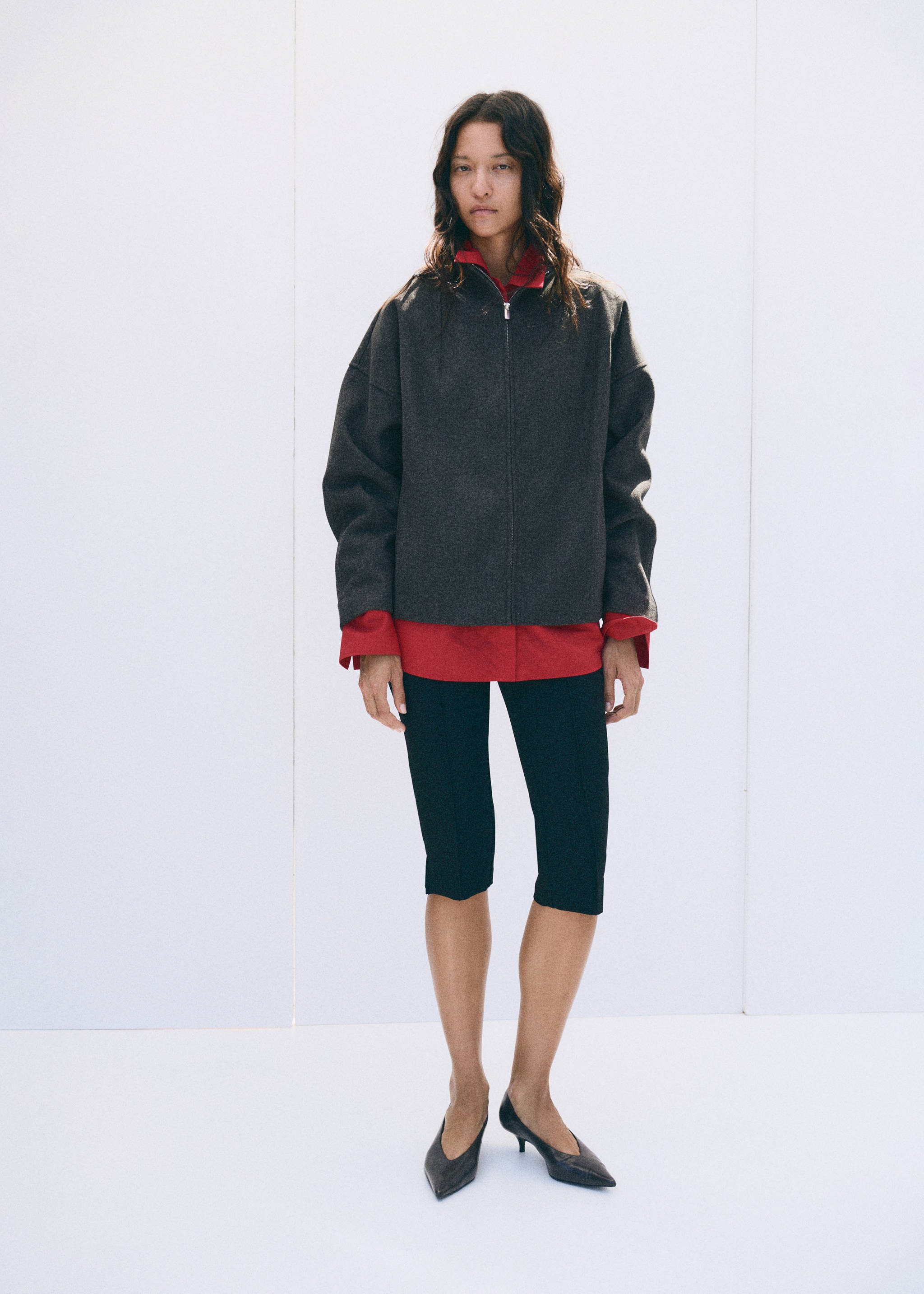 Dark grey zip-up jacket worn over a red shirt and dark trousers.