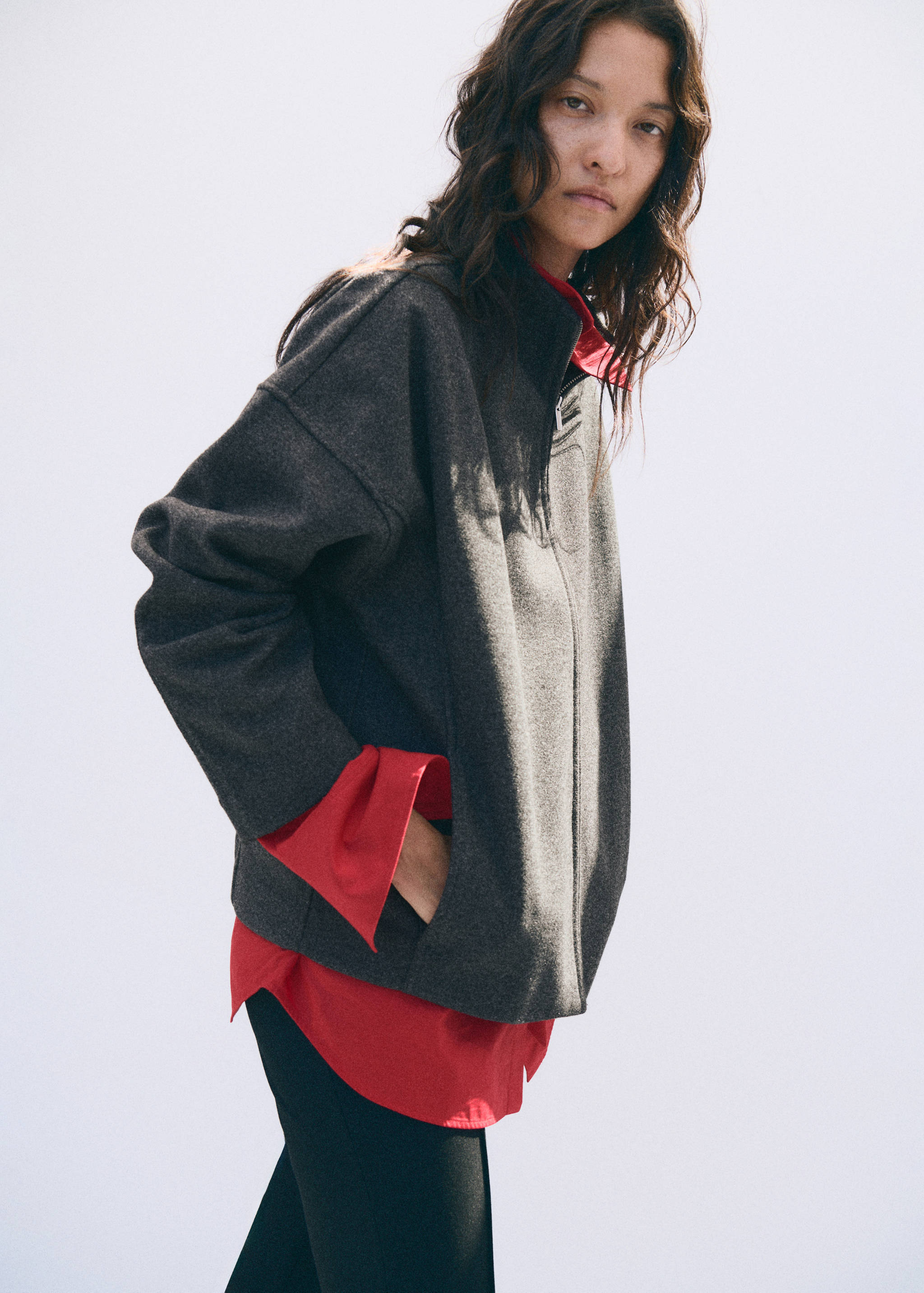 Dark grey zipped jacket with a high collar, worn over a red shirt.