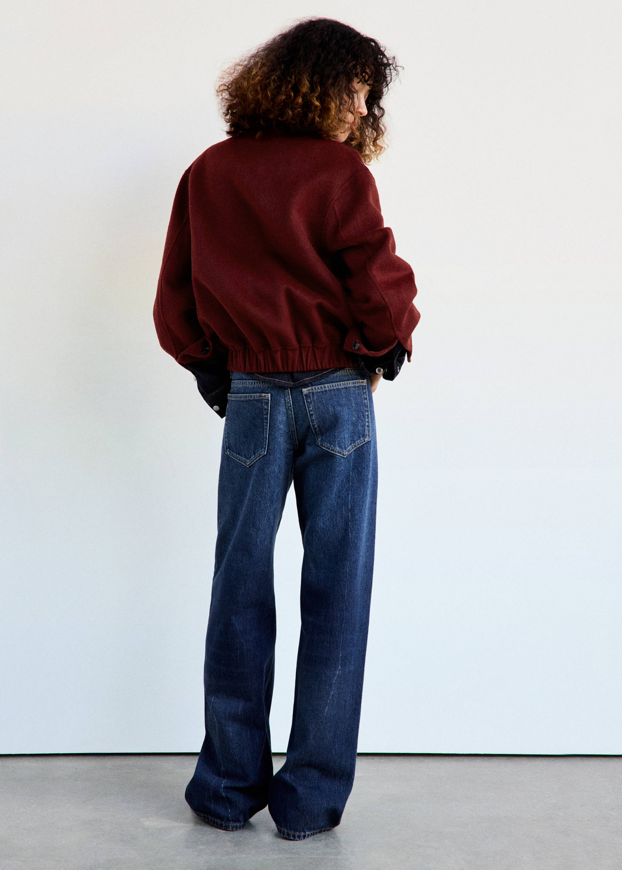 Burgundy jacket from the back with ribbed hem, worn with blue trousers.