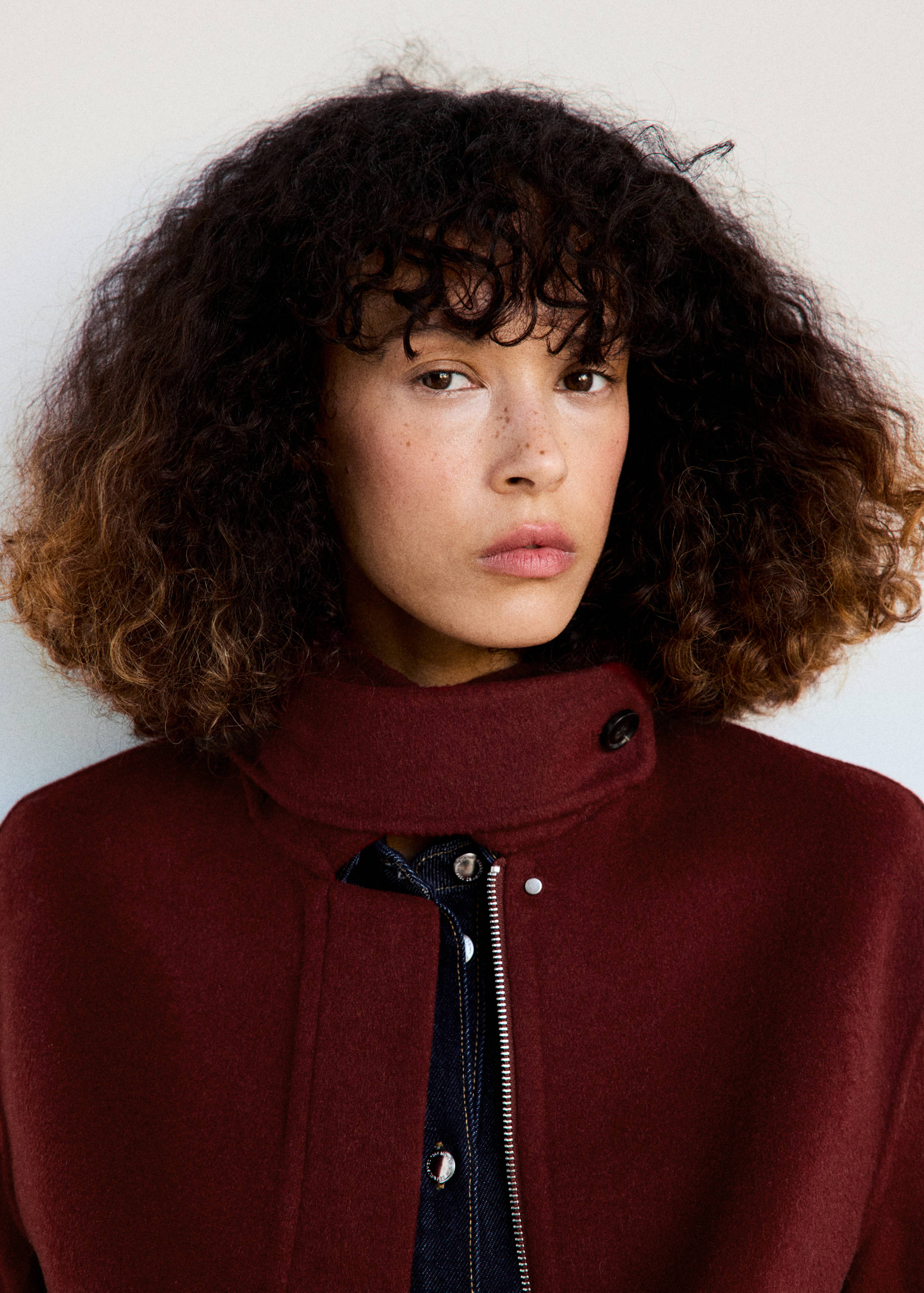 Burgundy jacket with a high collar and metal zip, worn with a dark denim shirt.