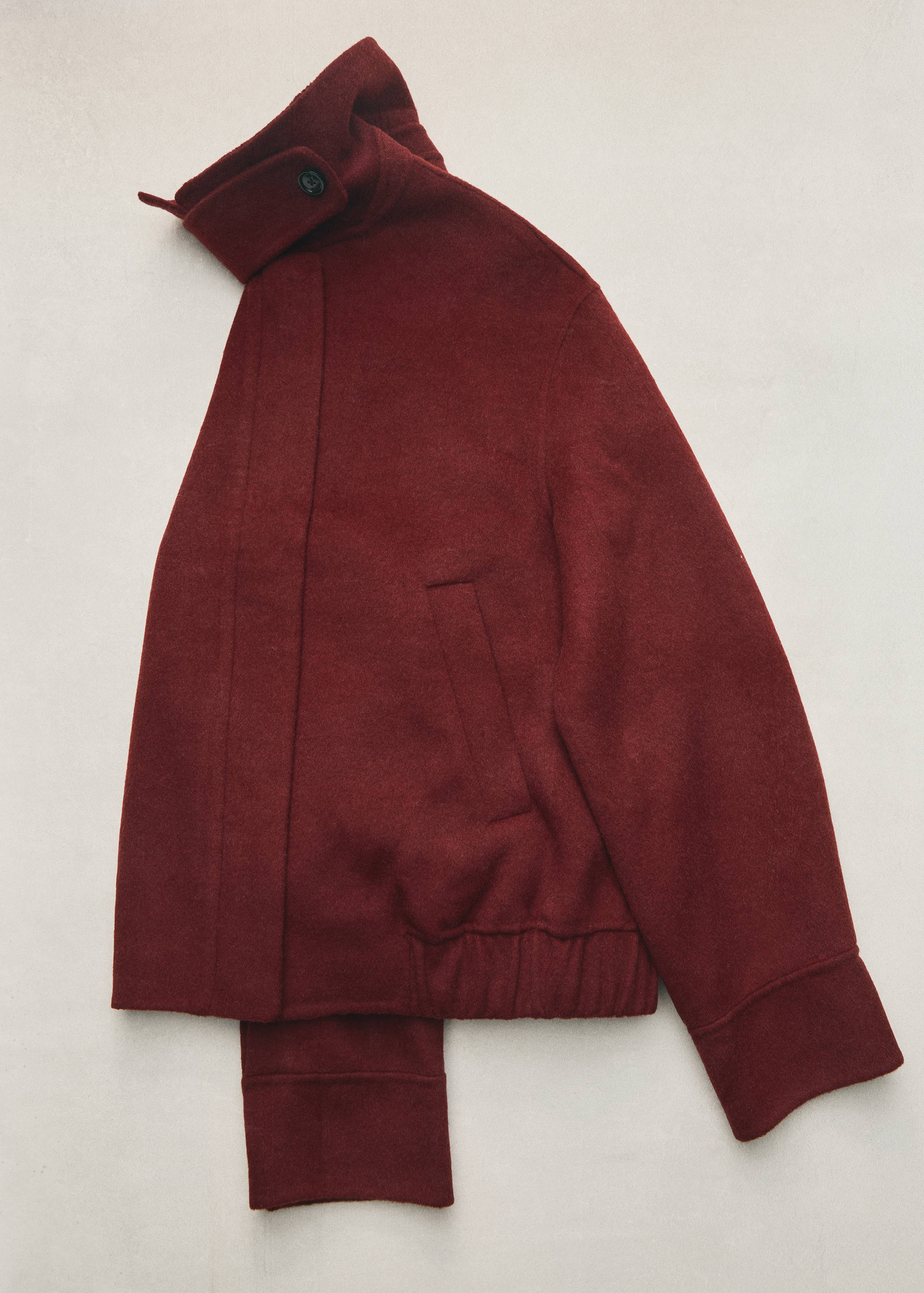 Burgundy short jacket with high collar and ribbed hem in a still life.