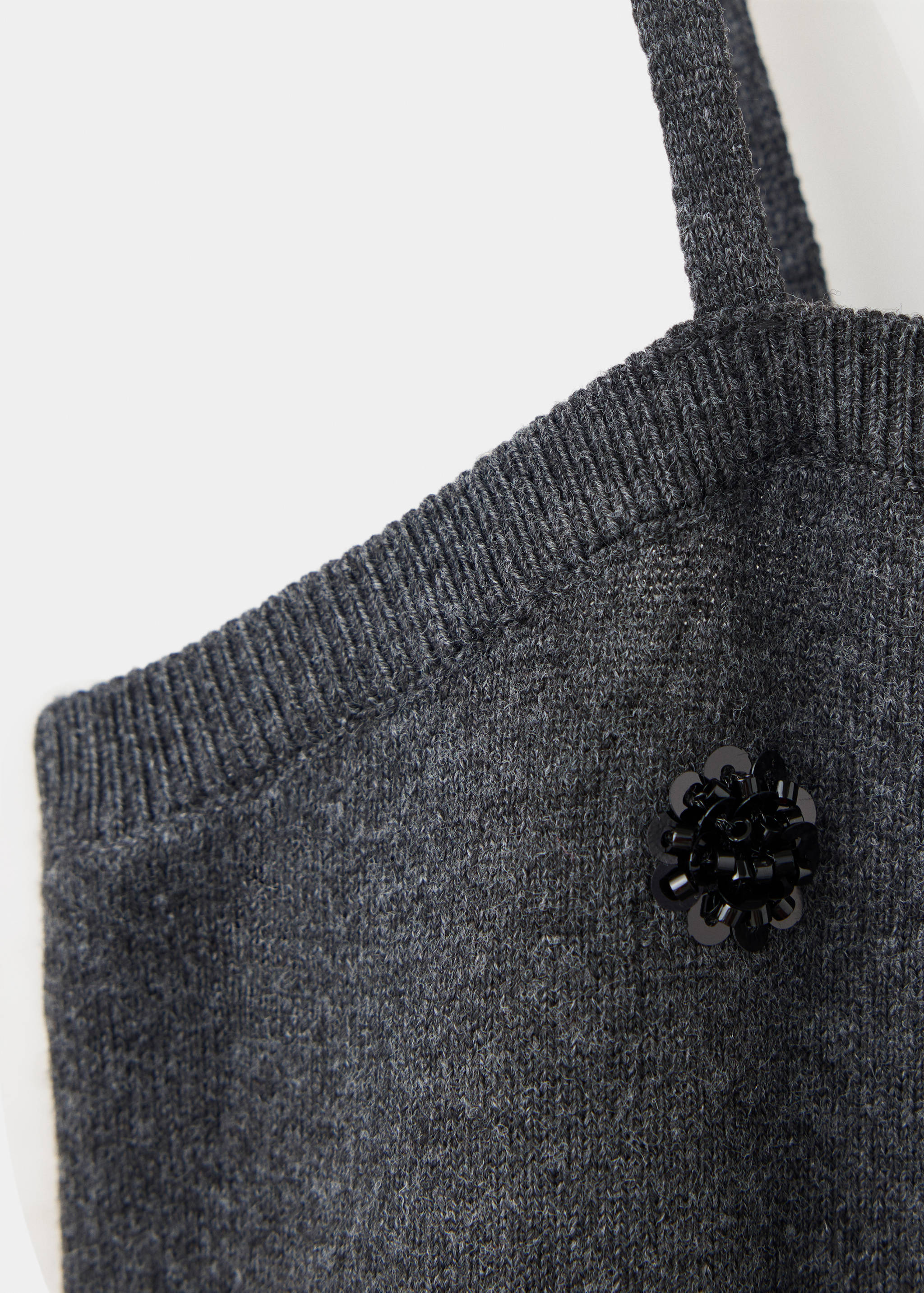 Dark grey knitted top detail with a beaded flower appliqué.
