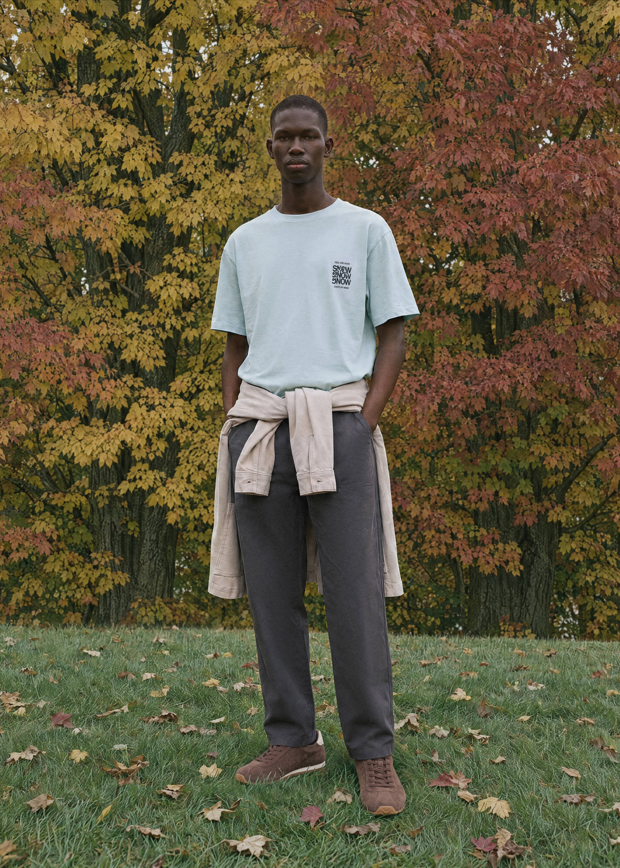Camiseta de manga corta azul claro con gráfico en el pecho, combinada con pantalones oscuros y camisa atada a la cintura.