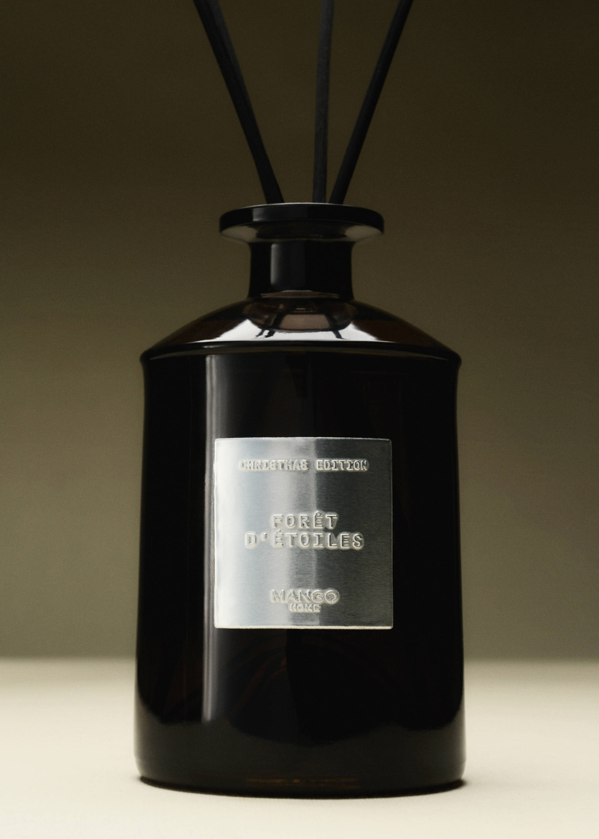 Dark glass reed diffuser bottle with a silver label reading Forêt d'Étoiles and black reeds.