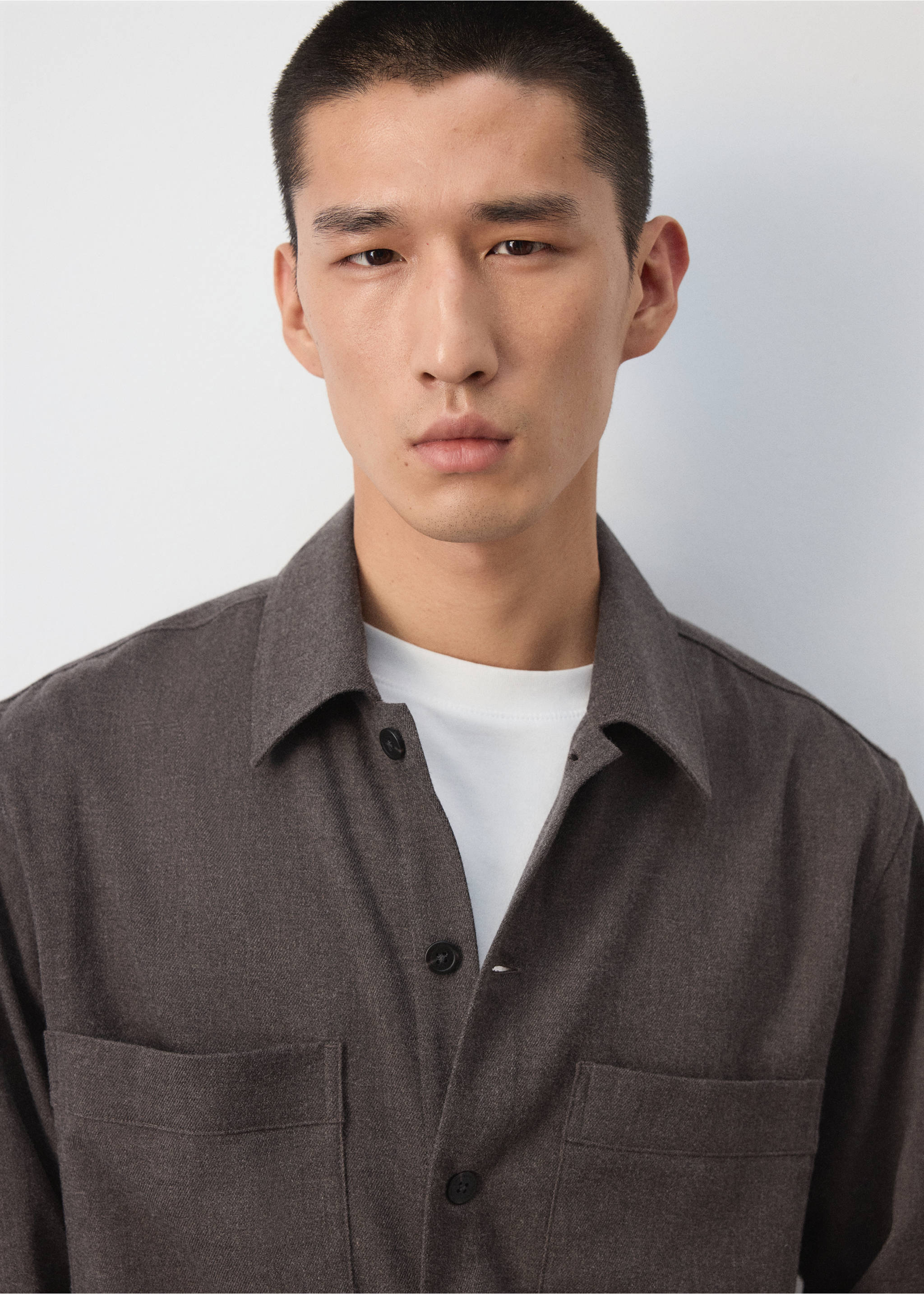 Close-up of a dark brown overshirt with chest pockets and dark buttons, worn over a white t-shirt., Brown. Ref: 37077884-00.