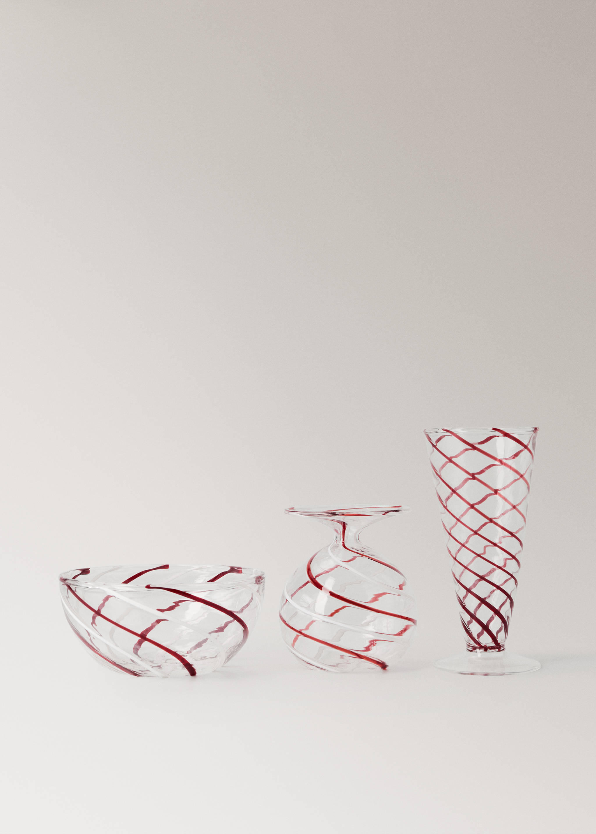 Set of clear glass items with a red swirl pattern, including a bowl, vase, and stemmed glass.
