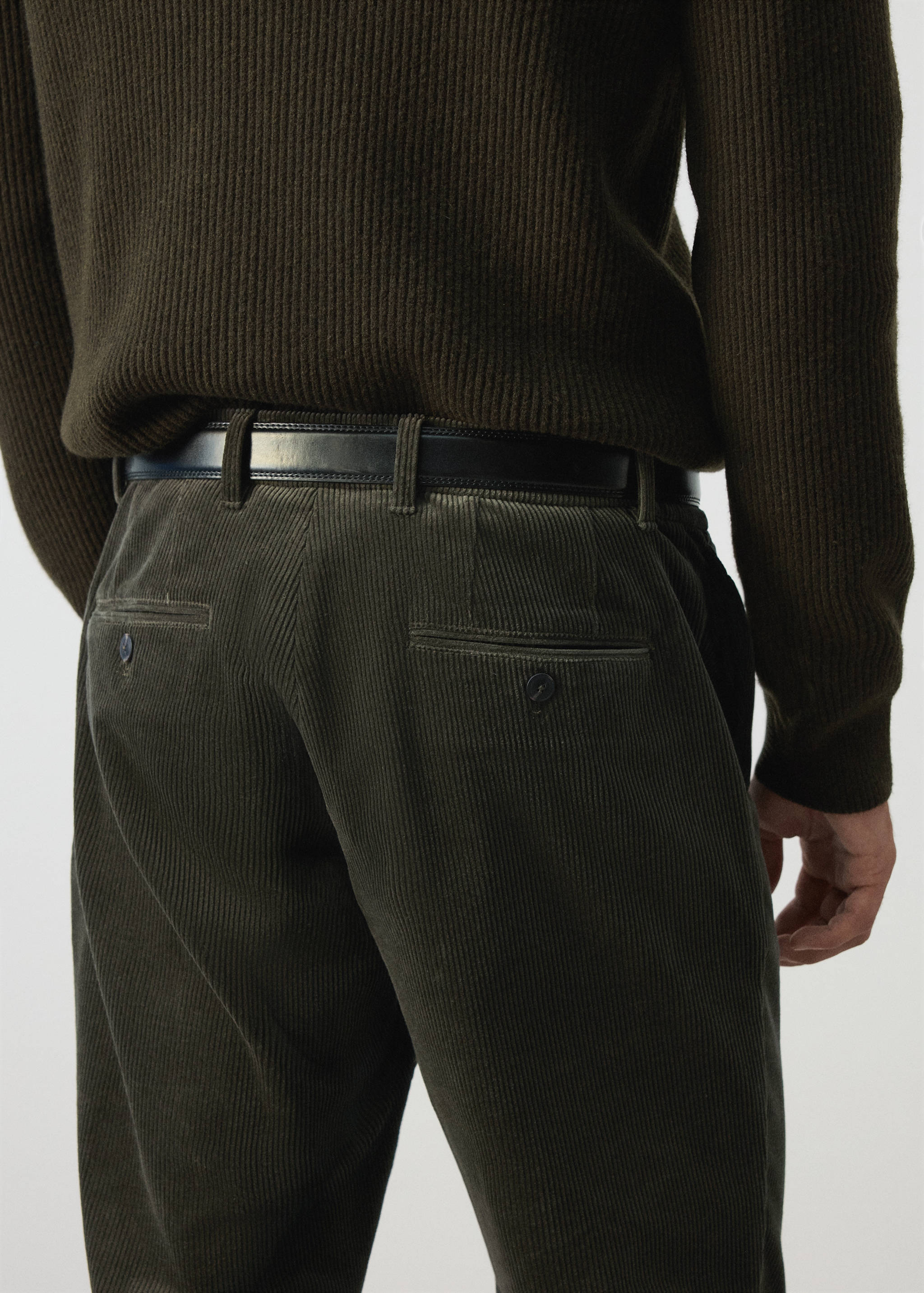 Olive green corduroy trousers with back welt pockets, worn with a belt.