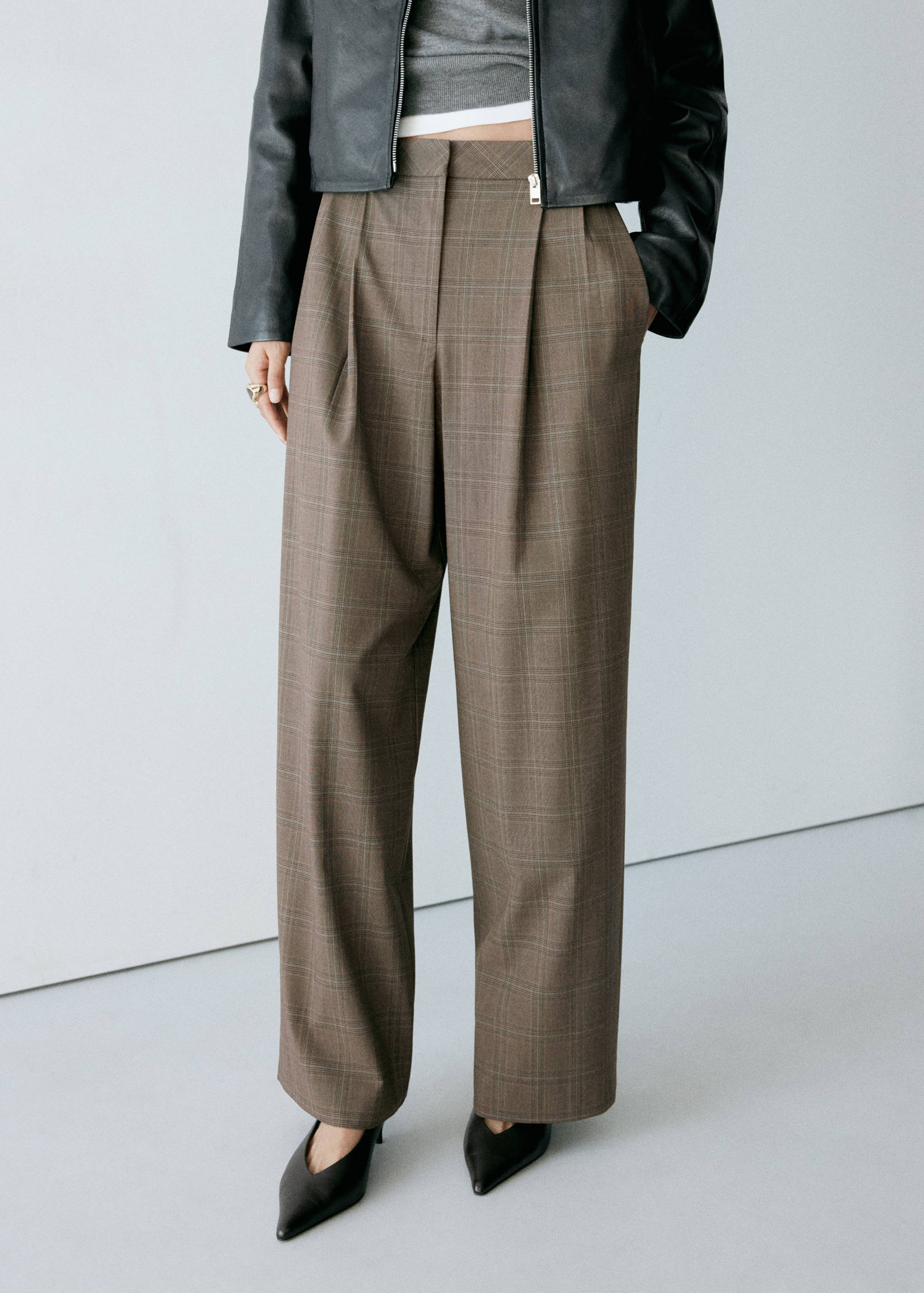 Brown checked high-waisted wide trousers with front pleats, styled with a black jacket.