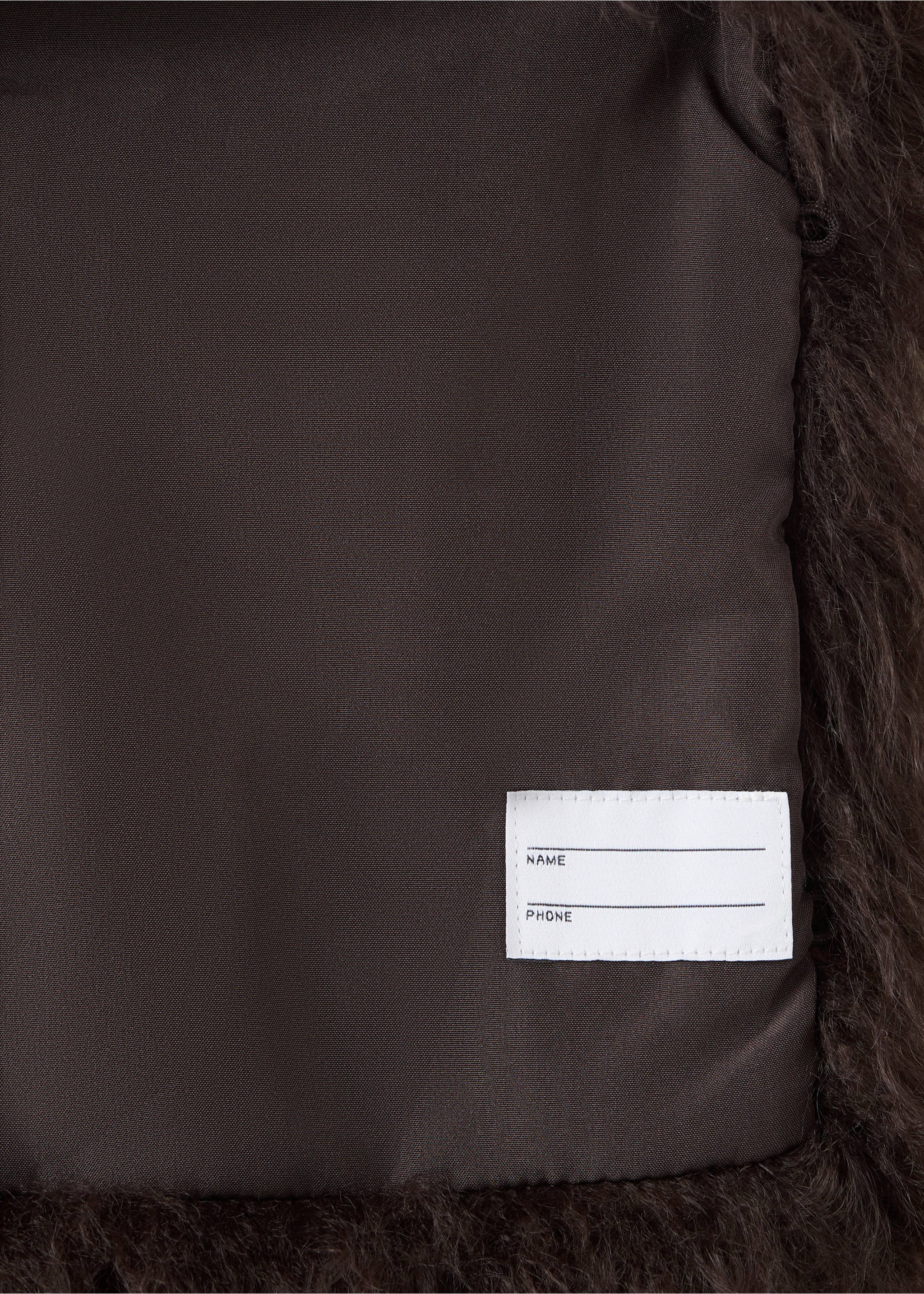 Close-up of a kids' brown outer vest showing the inner lining and name tag., Chocolate. Ref: 37077904-00.