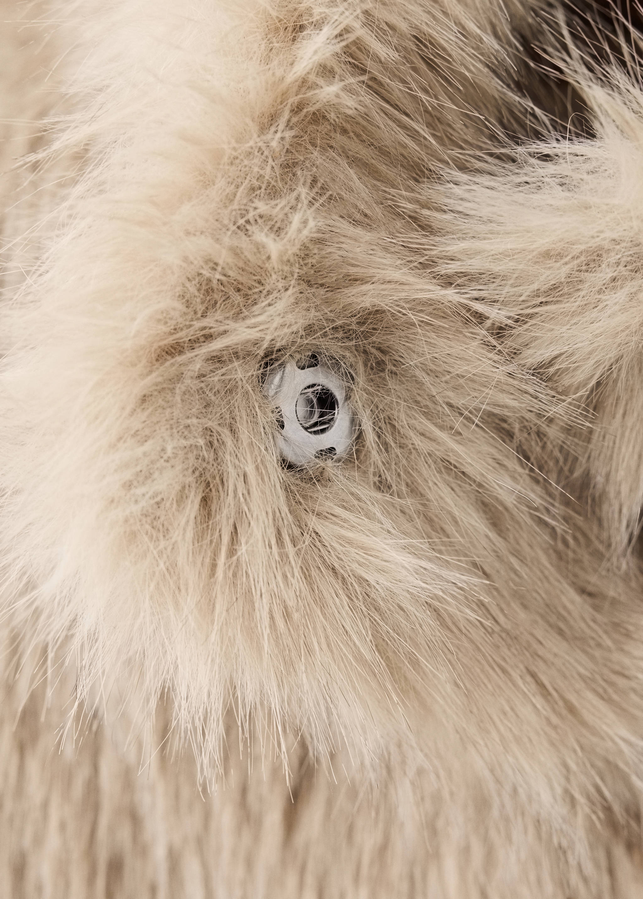 Close-up of a beige faux-fur coat detail showing the plush texture and fastener.