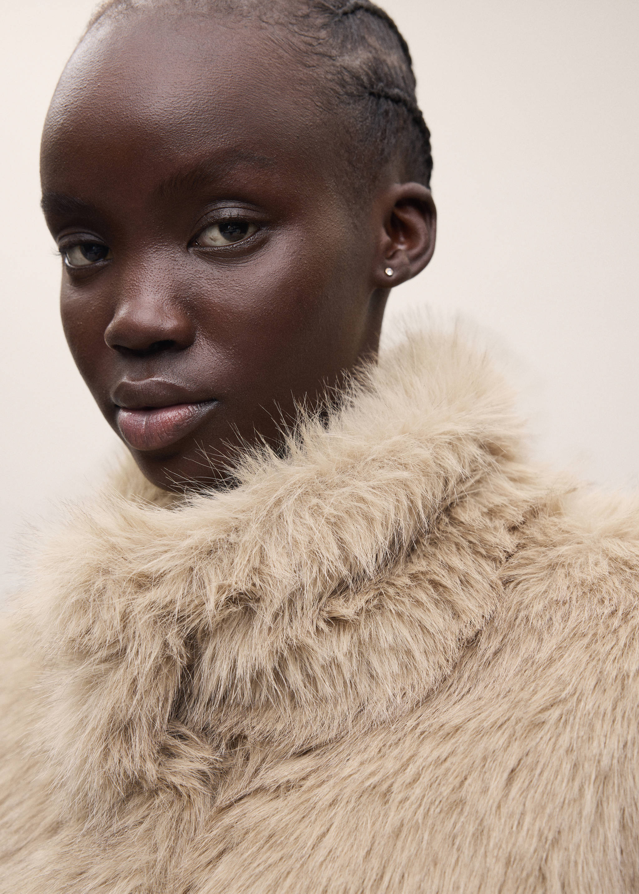 Close-up of a model wearing a beige faux-fur coat with a high collar.