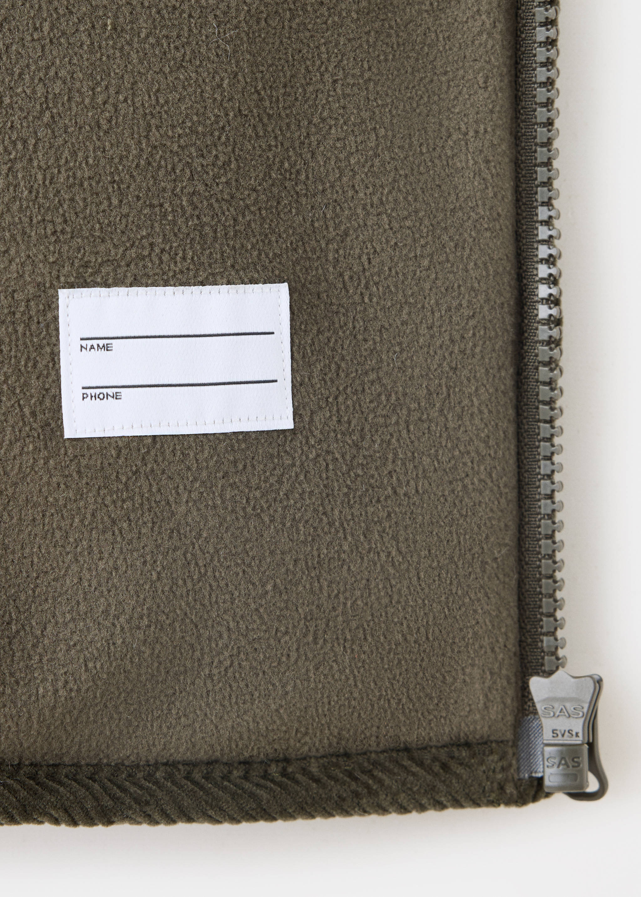 Close-up of olive green fleece jacket interior with personal label and zipper