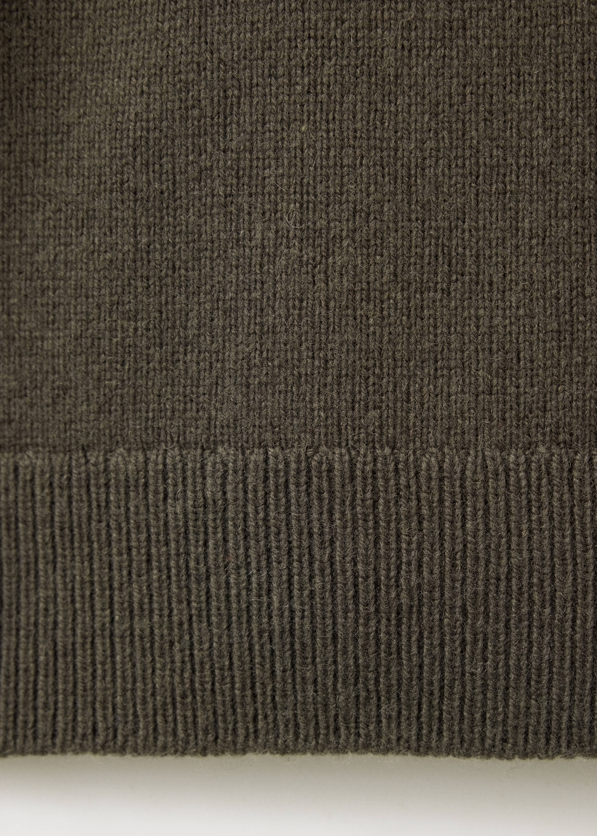 Close-up of the ribbed hem and fine knit texture of a dark khaki green sweater.