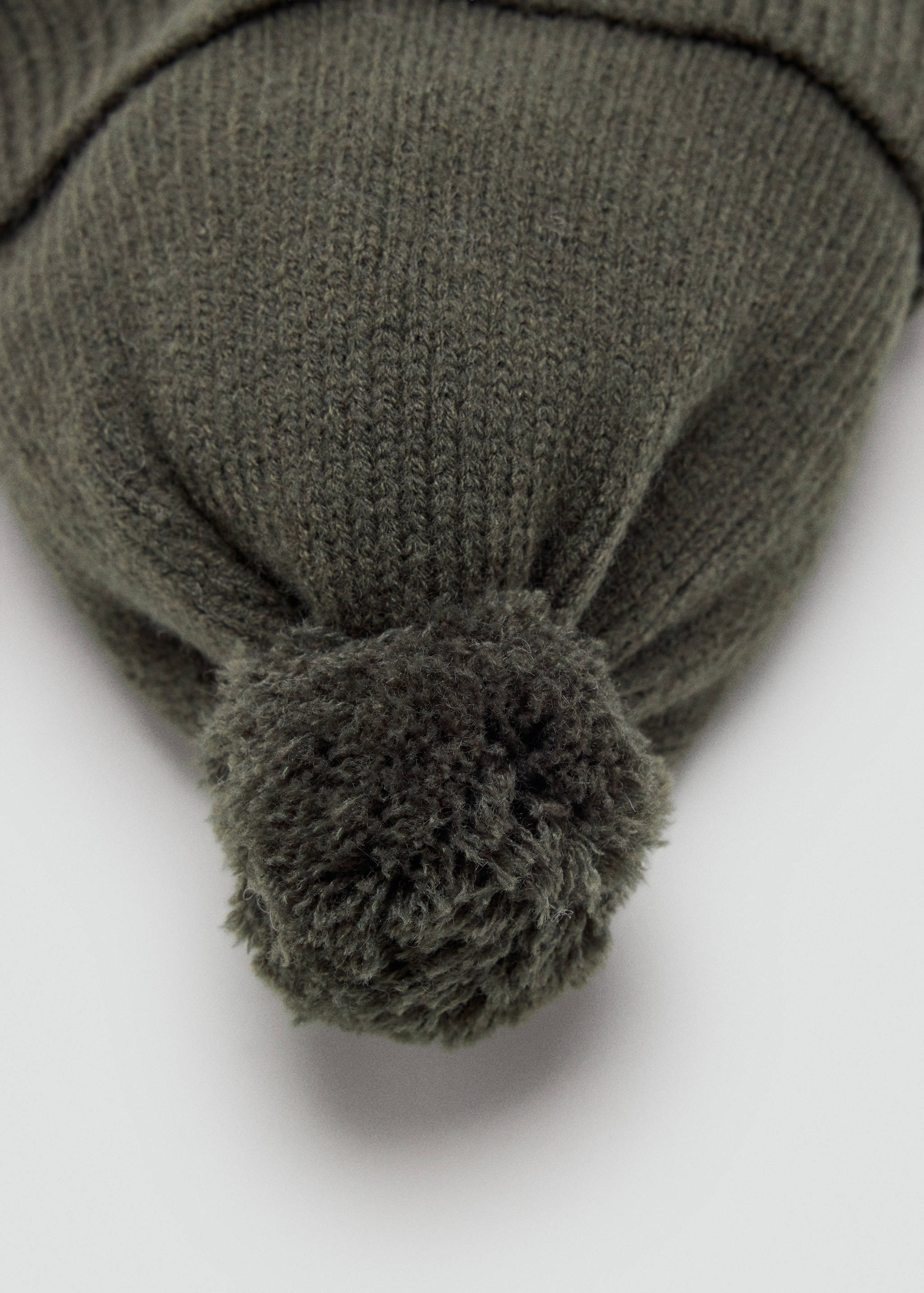 Close-up of the pom-pom detail on a khaki green knitted beanie.