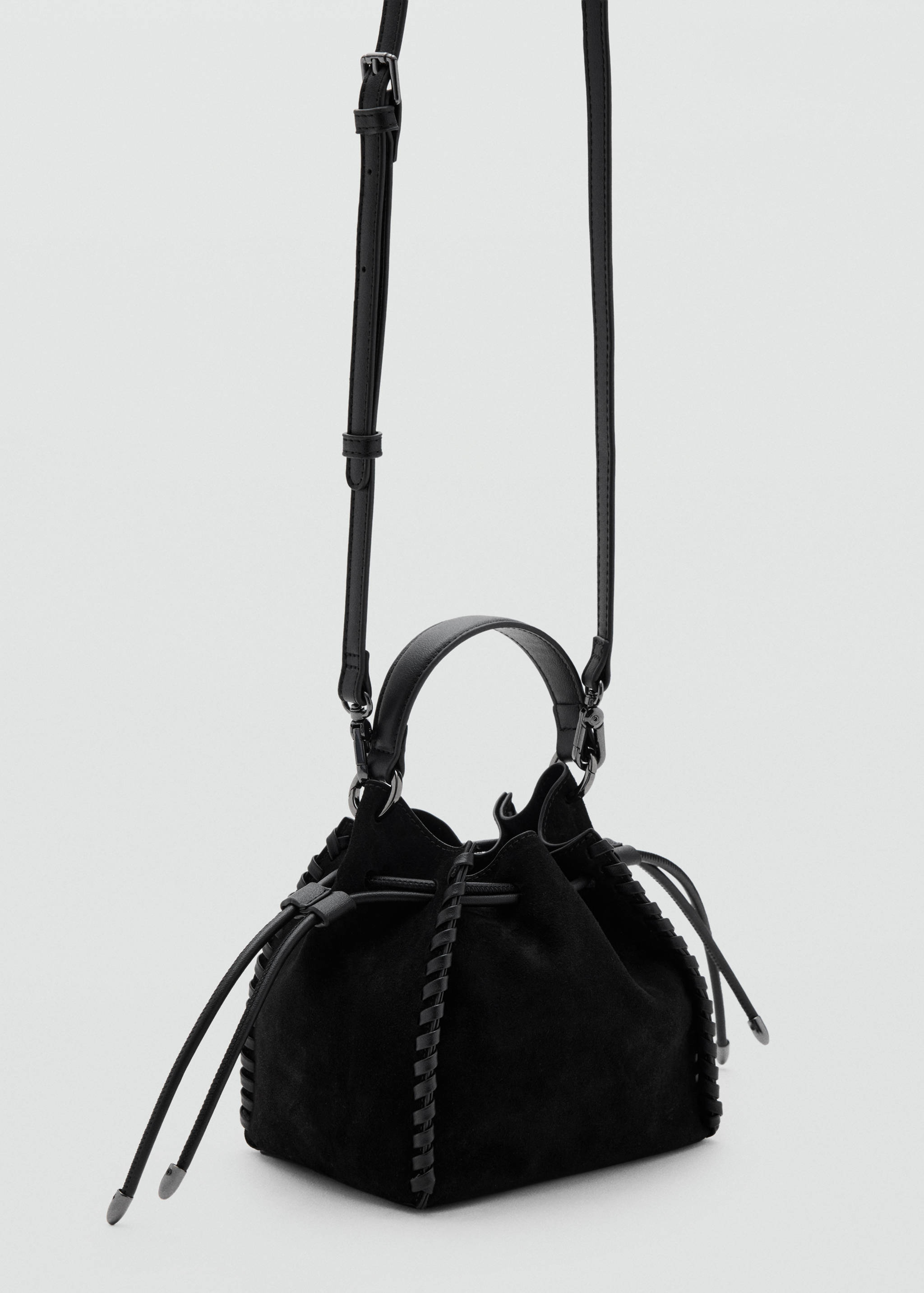 Black suede mini handbag with drawstring closure, whipstitch trim, top handle and long shoulder strap.