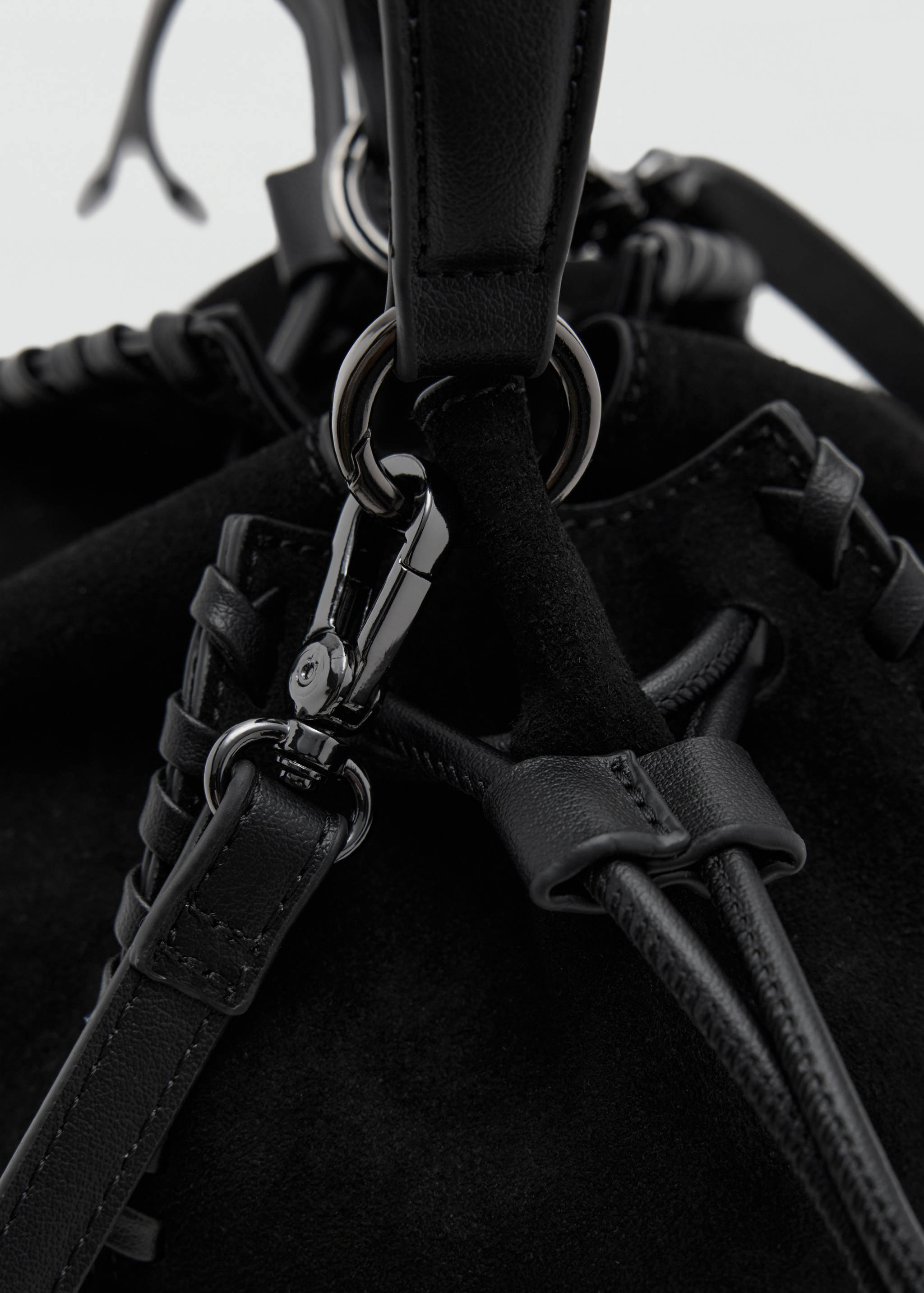 Close-up of a black mini bag showing strap hardware and braided trim detail.