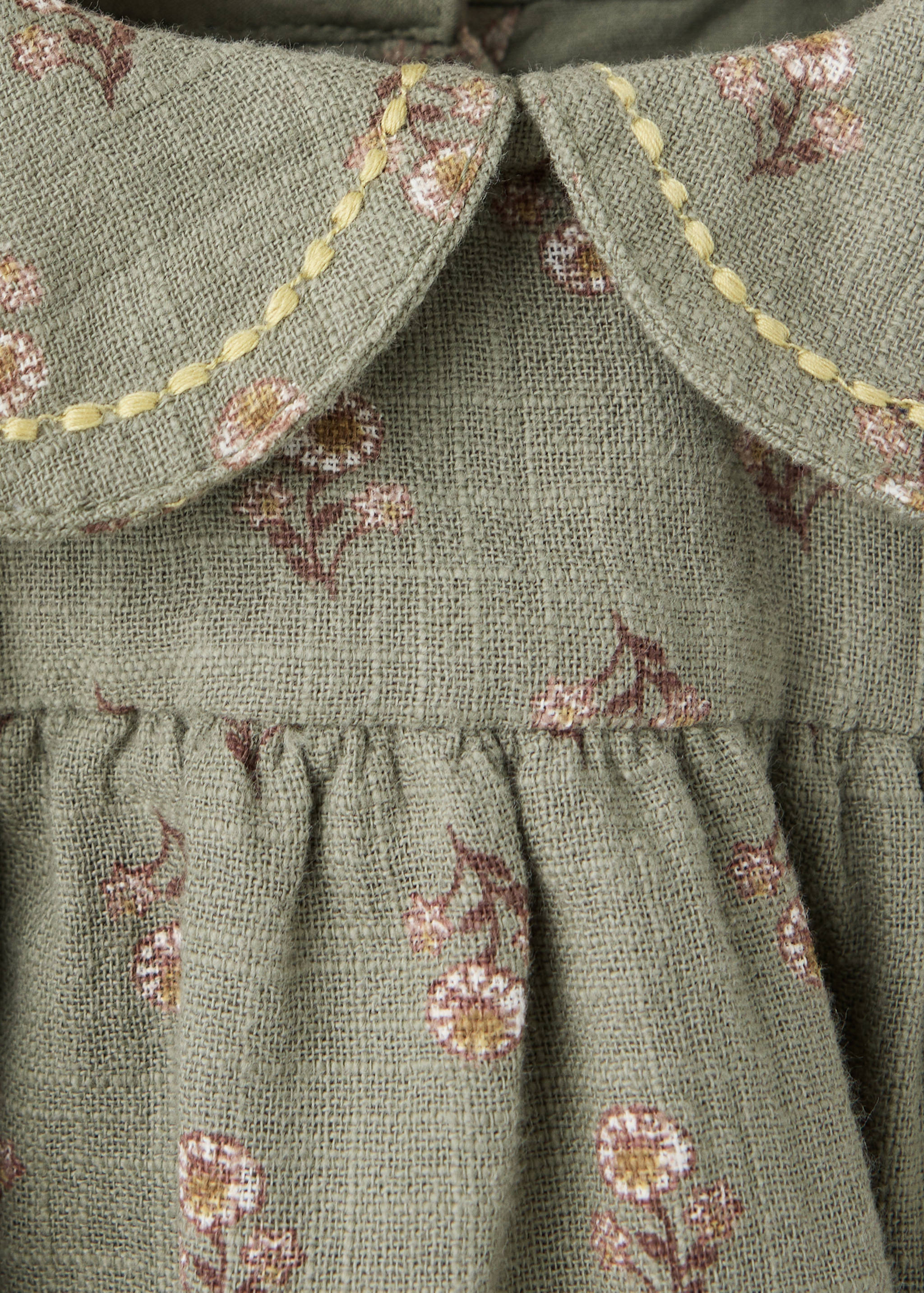 Olive green floral dress detail with a Peter Pan collar and yellow topstitching.