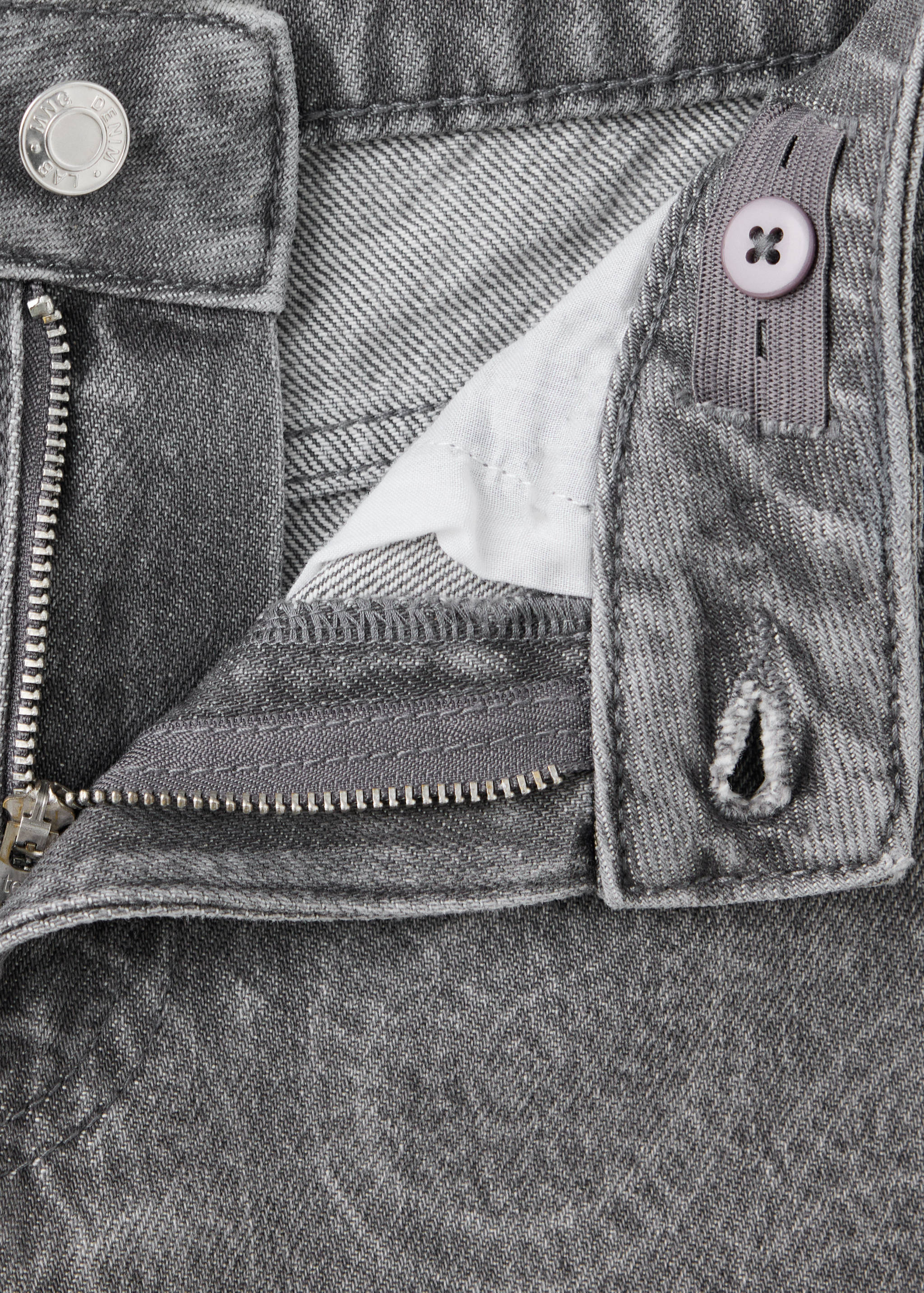 Close-up of grey denim trousers showing the waistband, zip fly, and button detail.