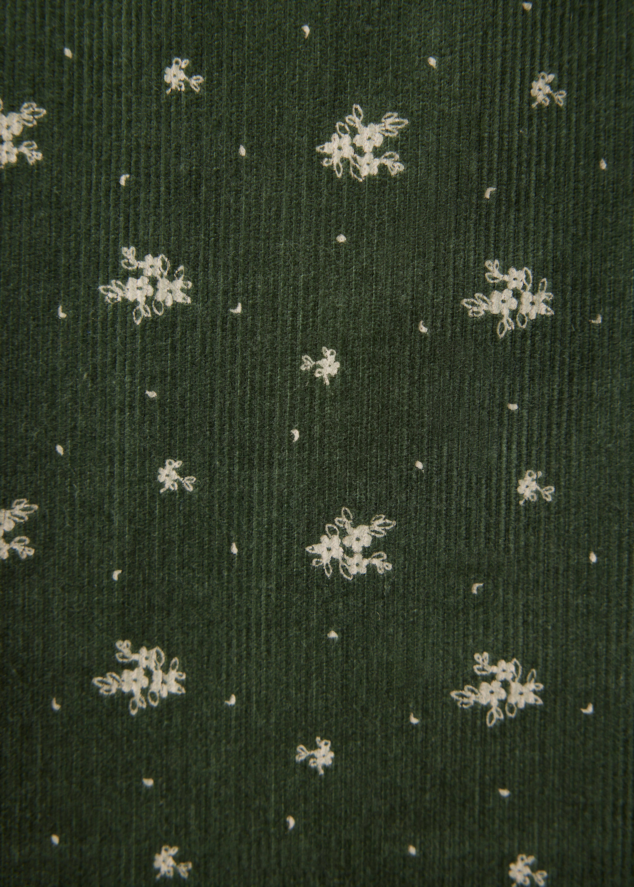 Tejido de pana verde oscuro con bordado de flores blancas.