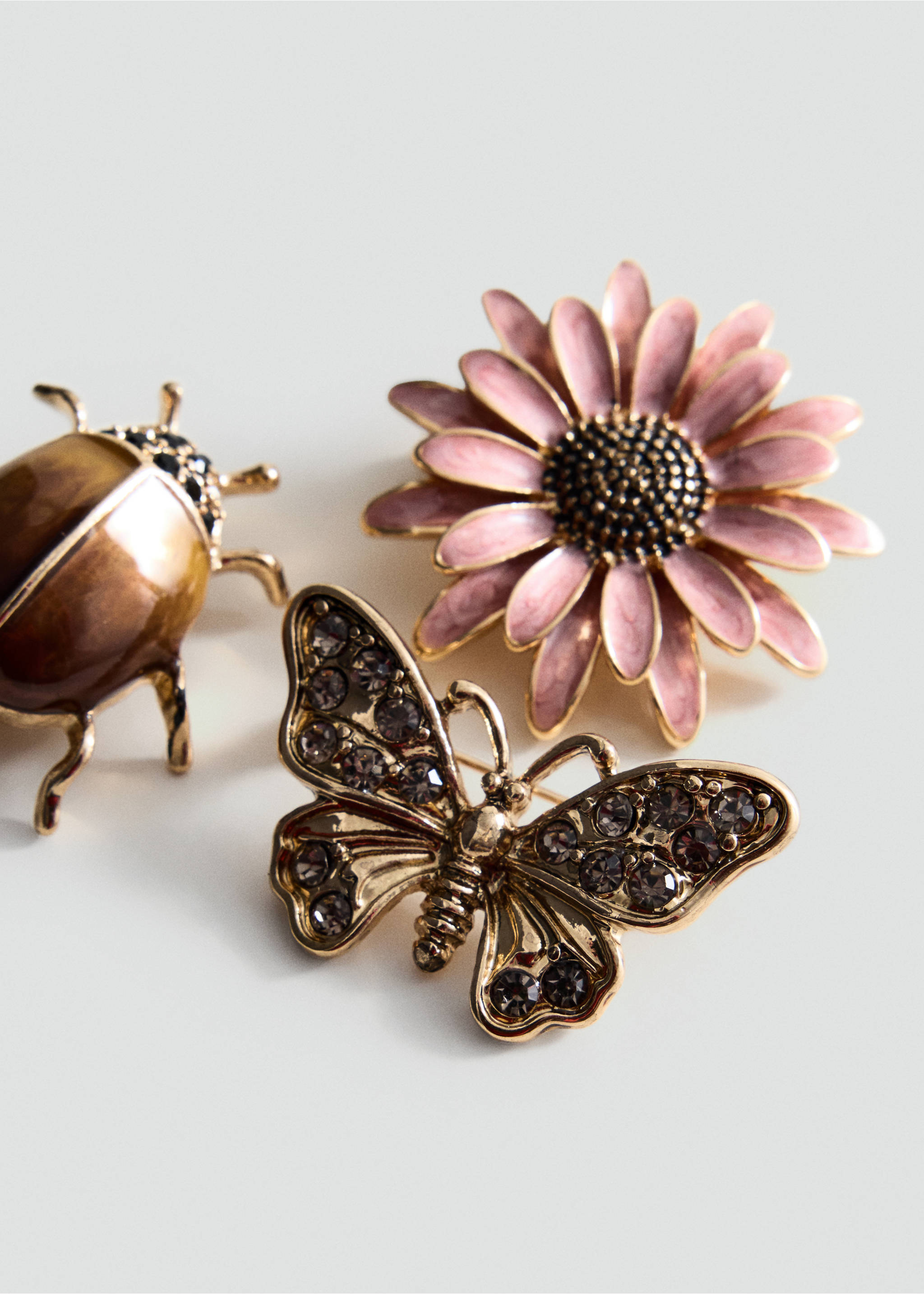 Close-up of three decorative metallic brooches featuring a pink flower, a brown beetle, and a crystal butterfly., Gold. Ref: 37077944-00.