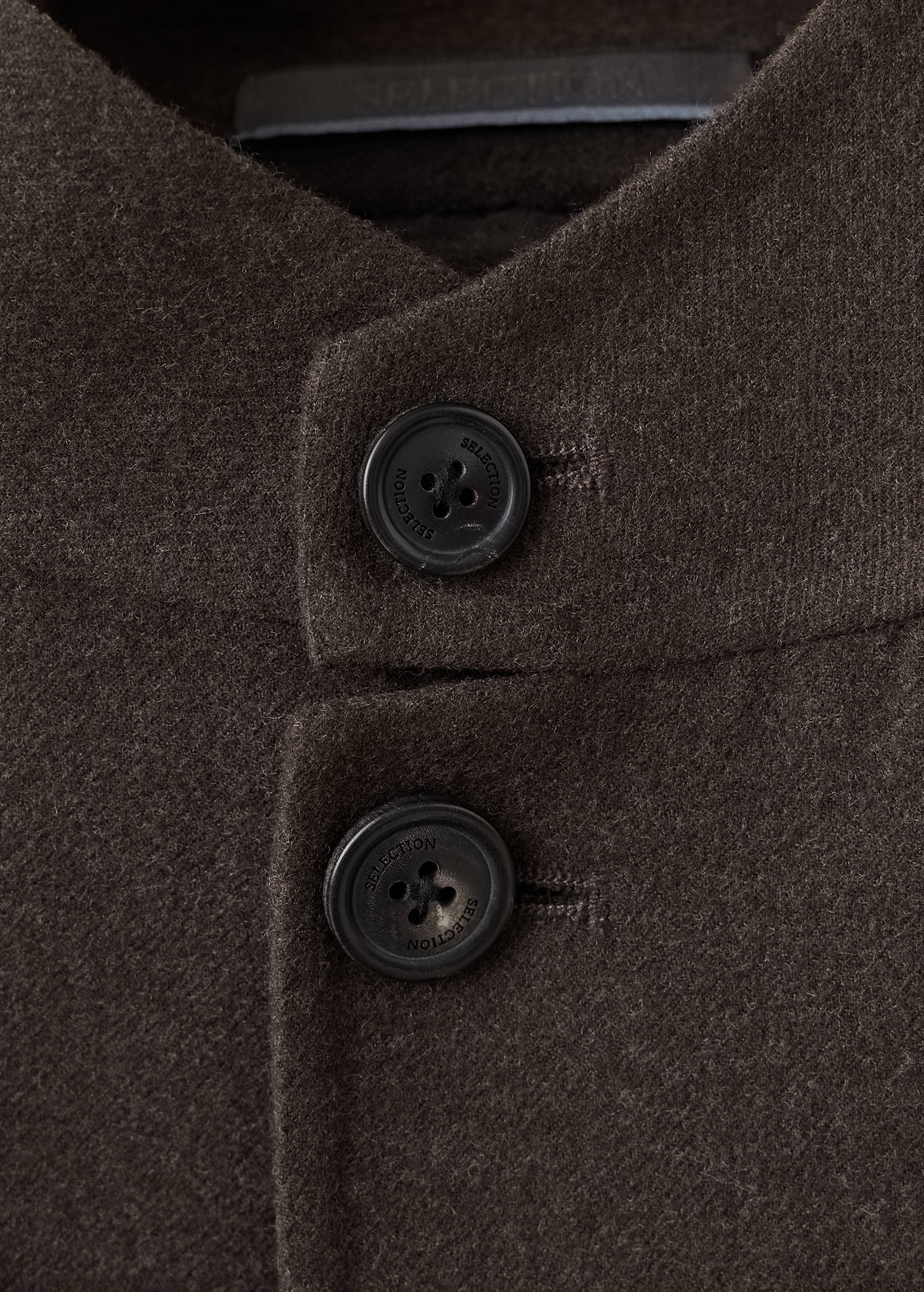 Close-up of a dark brown blazer showing button detail and collar.
