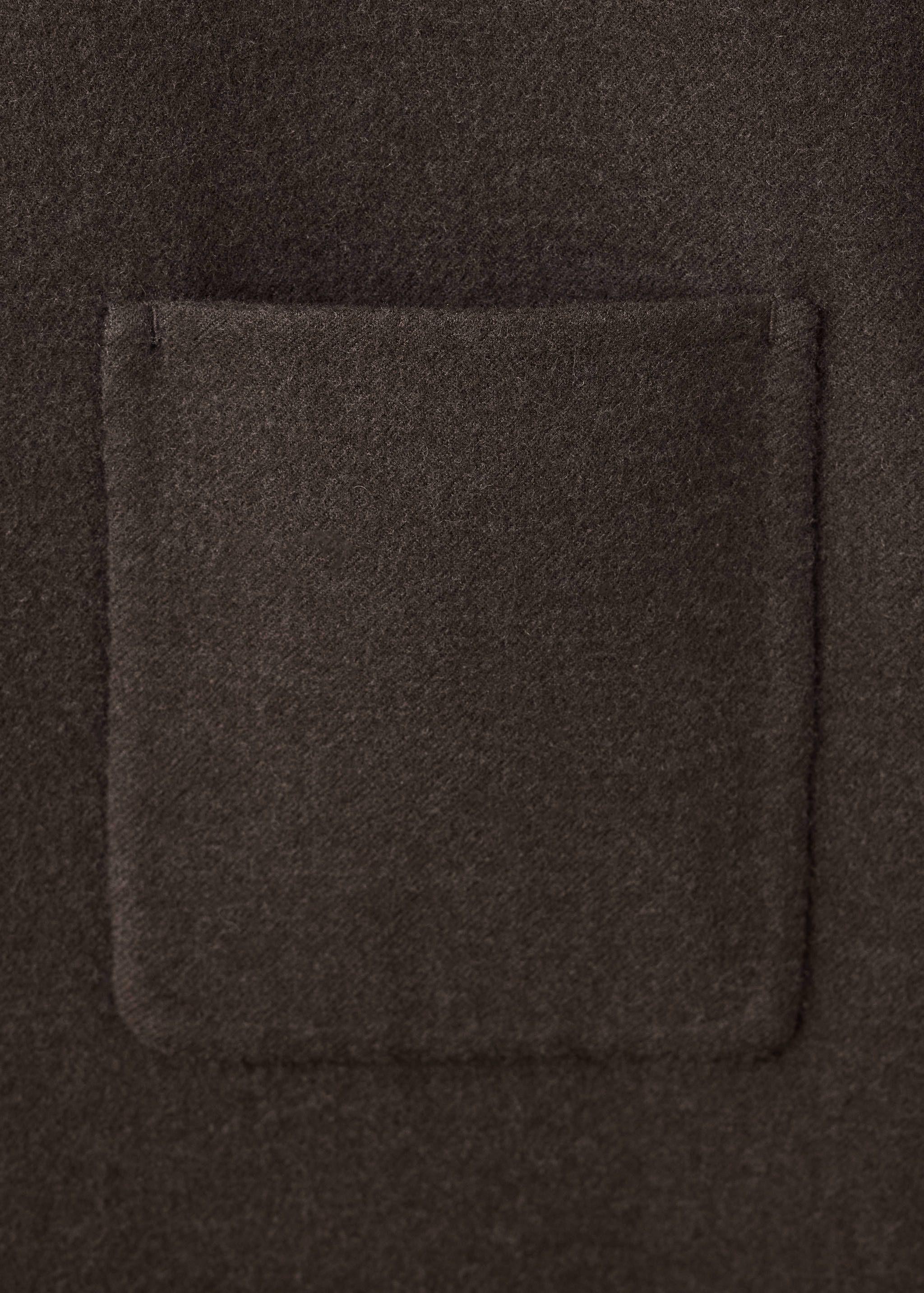 Close-up of the textured fabric and patch pocket on a dark brown blazer.