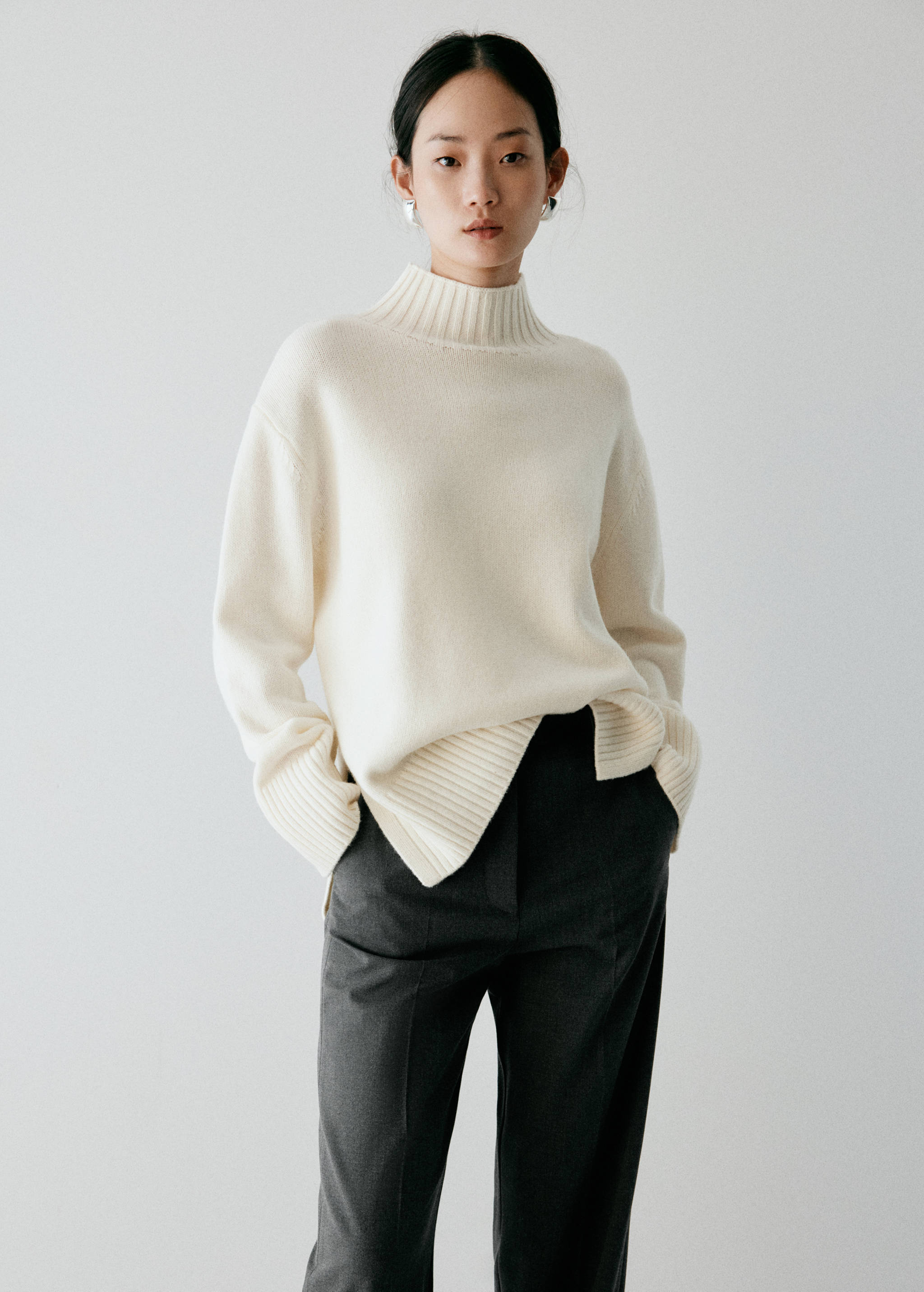 Dark grey trousers paired with a cream high-neck jumper.