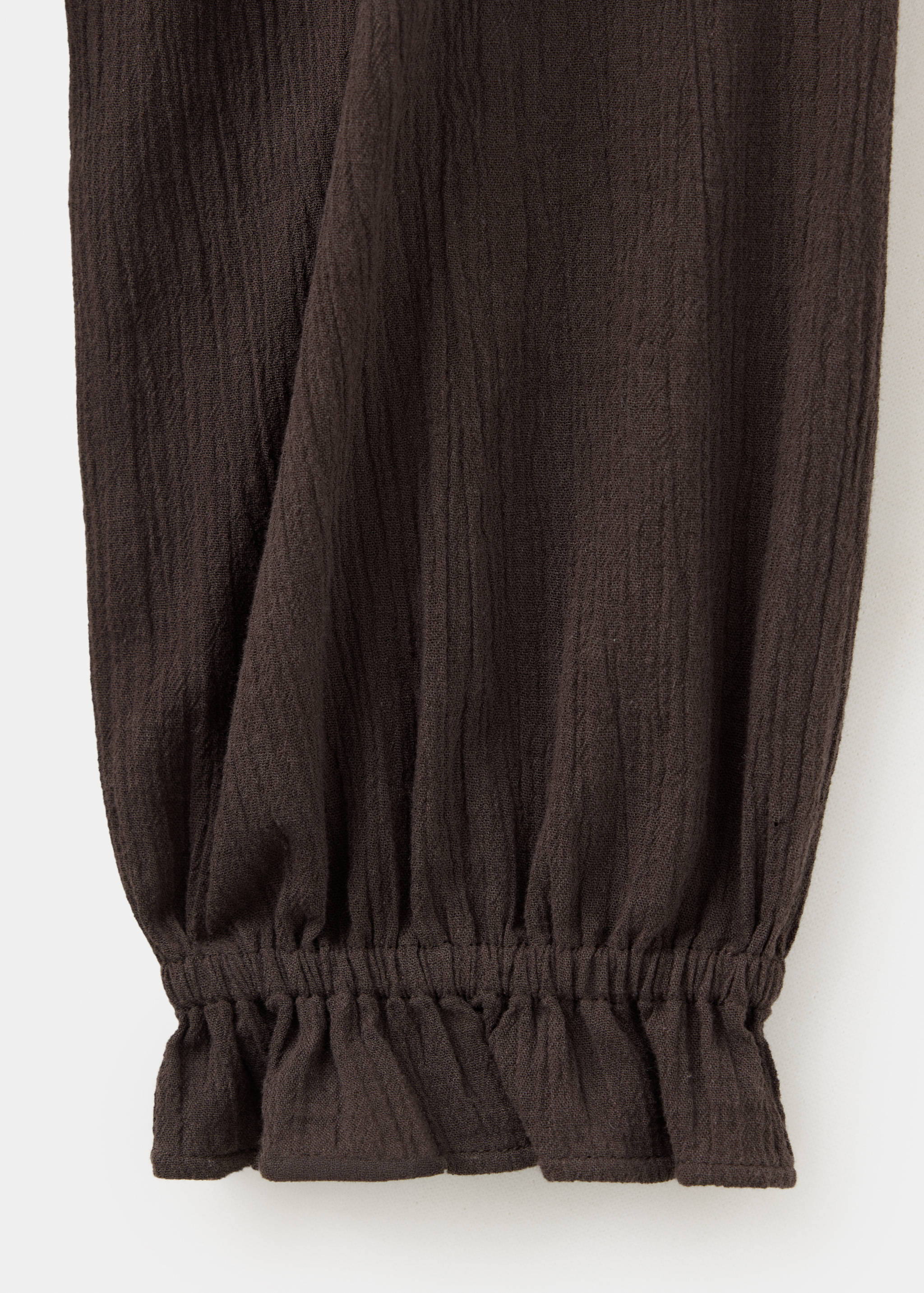 Close-up of the textured fabric and smocked cuff on a dark brown teen dress.