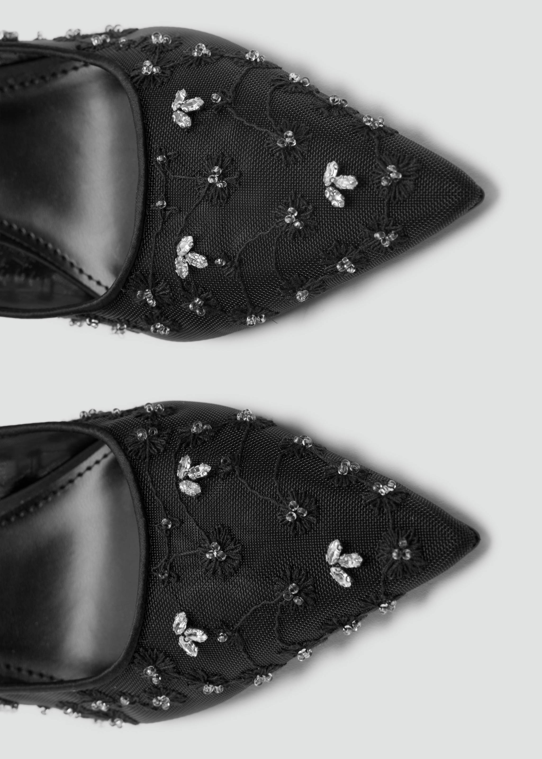 Close-up of black mesh shoes with pointed toes and crystal floral beading.