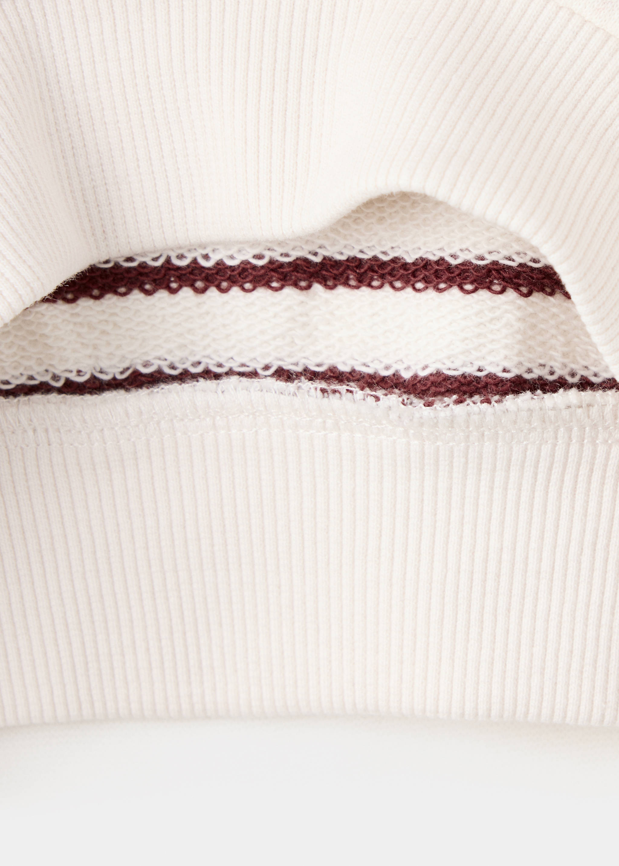 Close-up of off-white sweatshirt fabric with ribbed hem and striped lining.