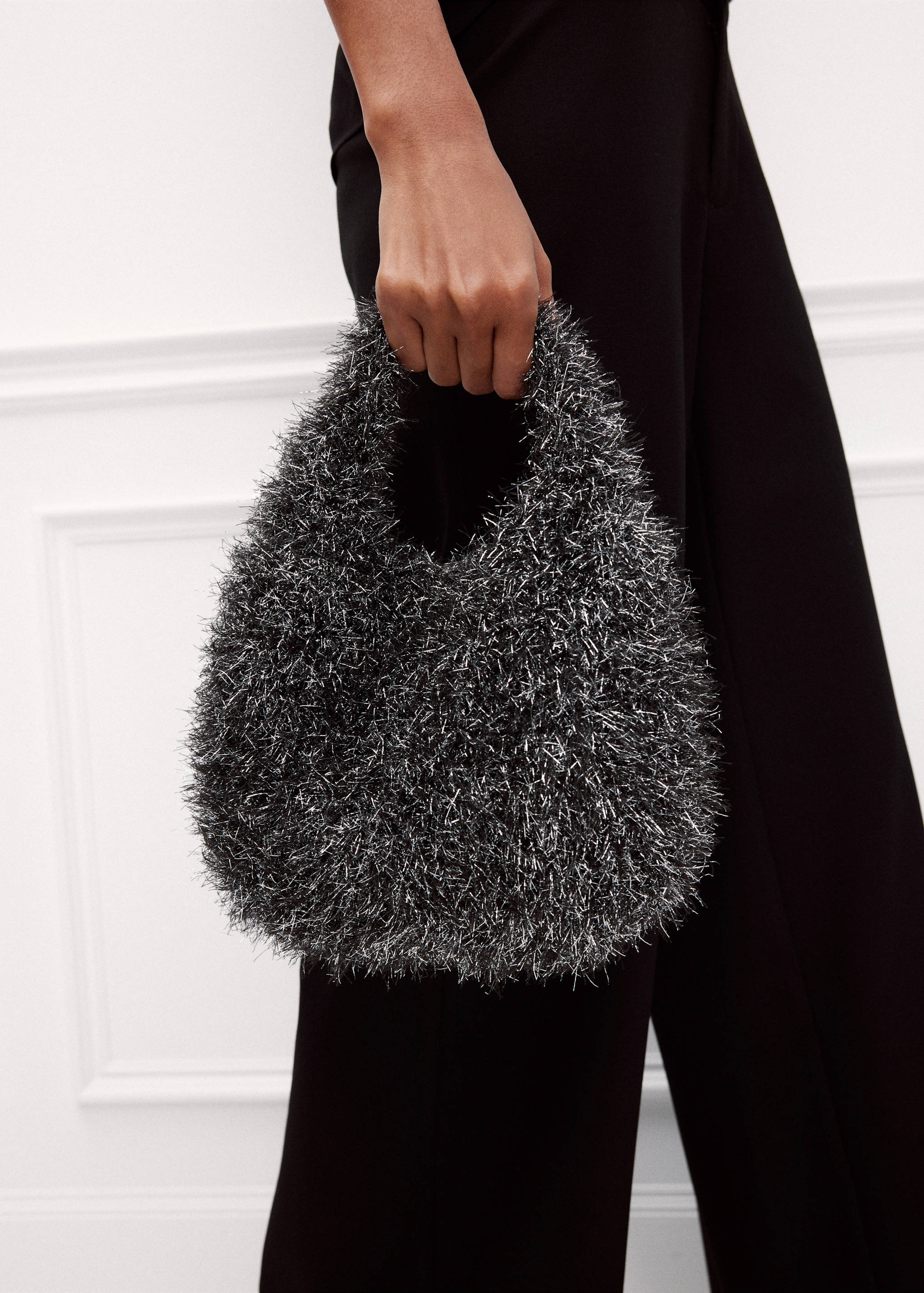 Mini bolso negro y plateado con textura, diseño redondeado y asa abierta.