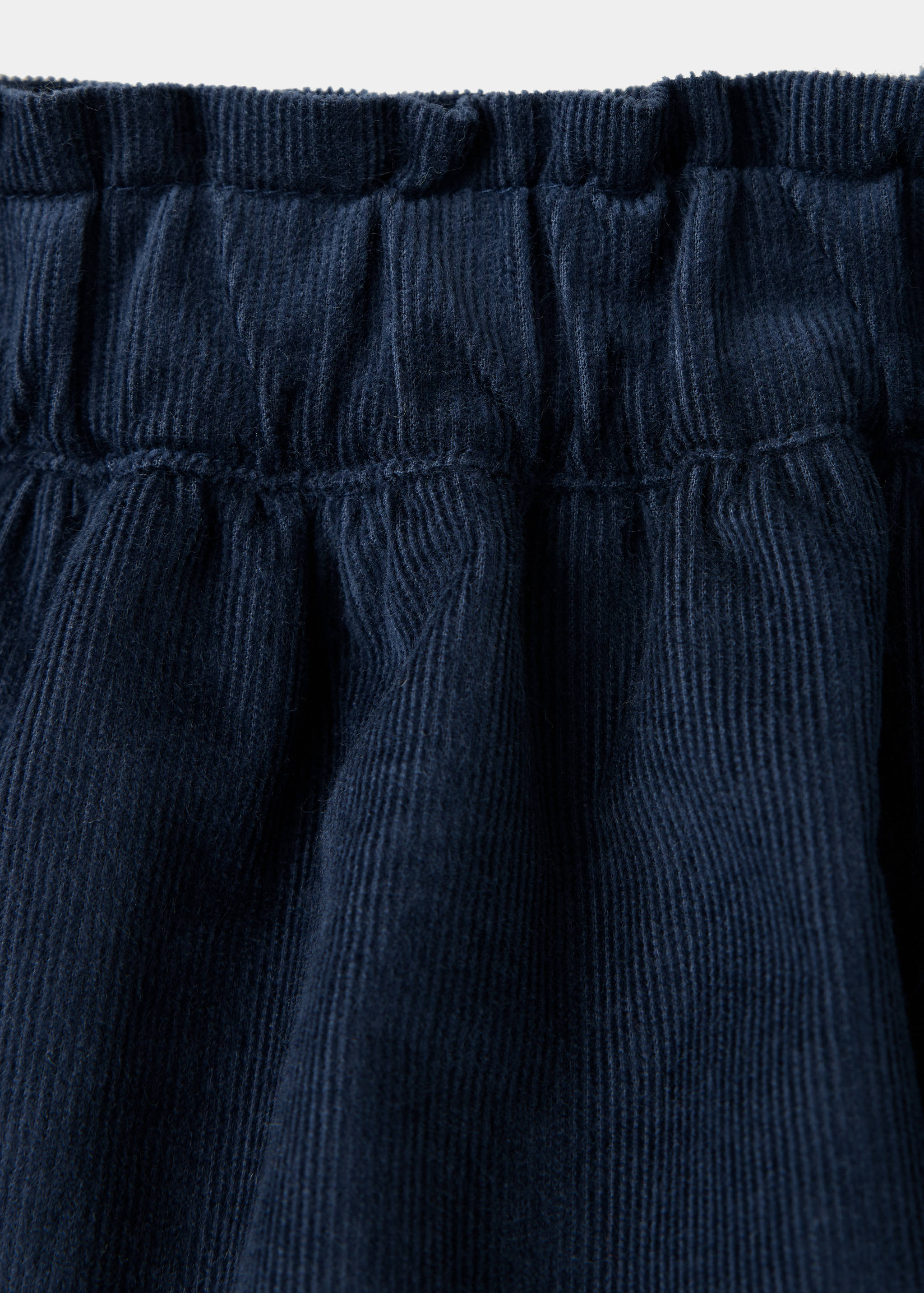 Detalle de la pretina de una falda de pana azul oscuro con un volante fruncido.